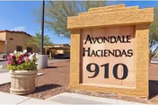 Stone entrance sign reads Avondale Haciendas 910 with potted flowers and desert landscaping.