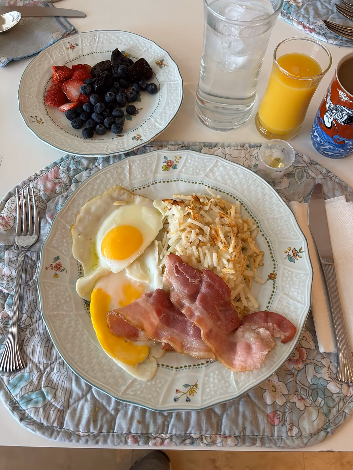 Breakfast on a dining table with eggs, bacon, hash browns, and a berry plate.