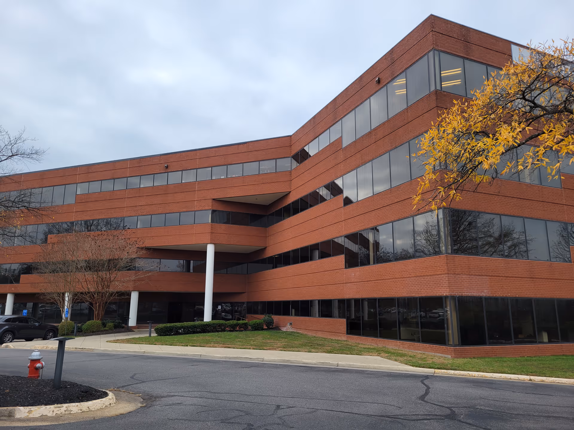 Red-brick, multi-story building with expansive windows and nearby trees in a parking lot.