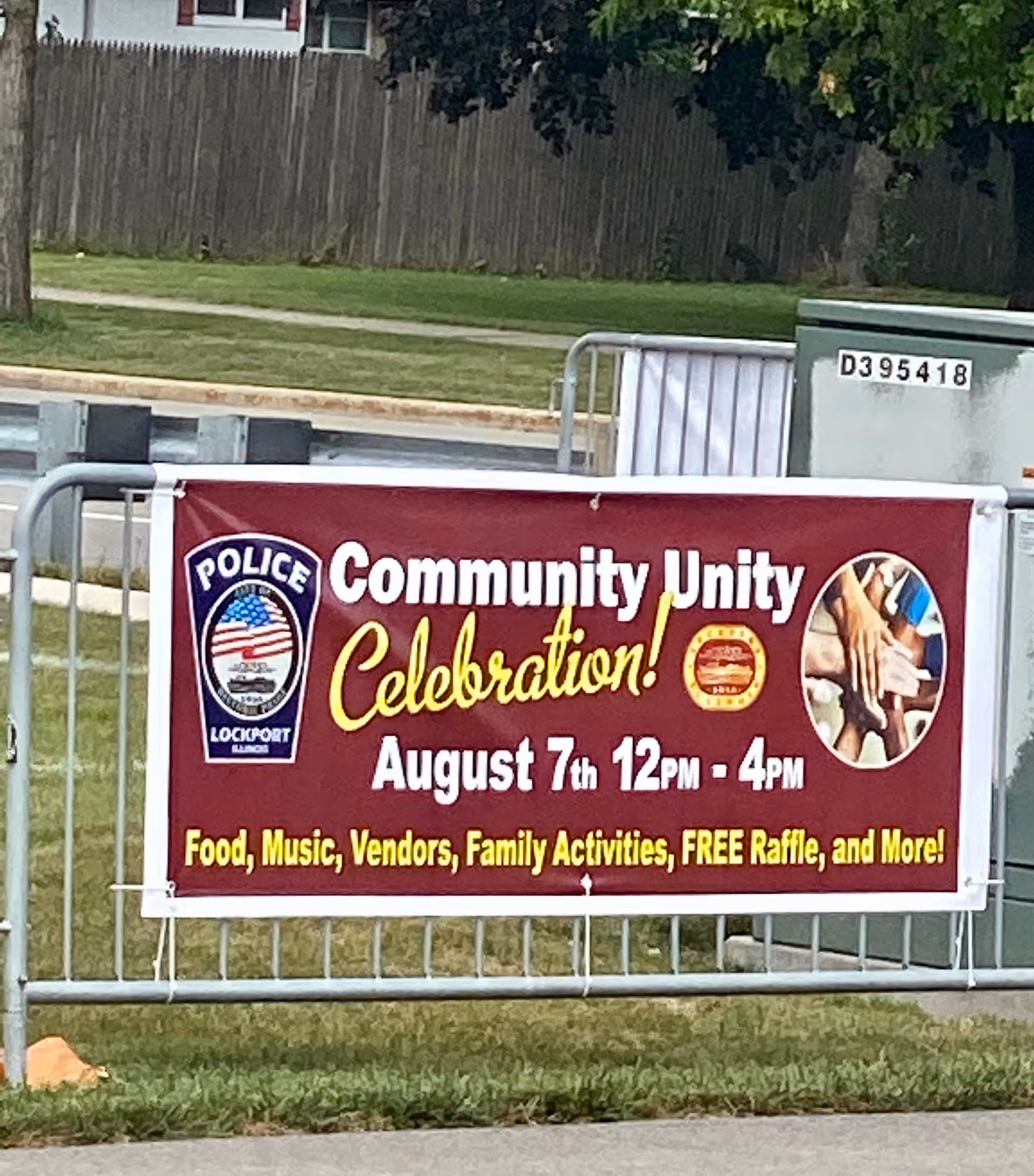 Large maroon Community Unity Celebration banner displayed on metal barriers outdoors.
