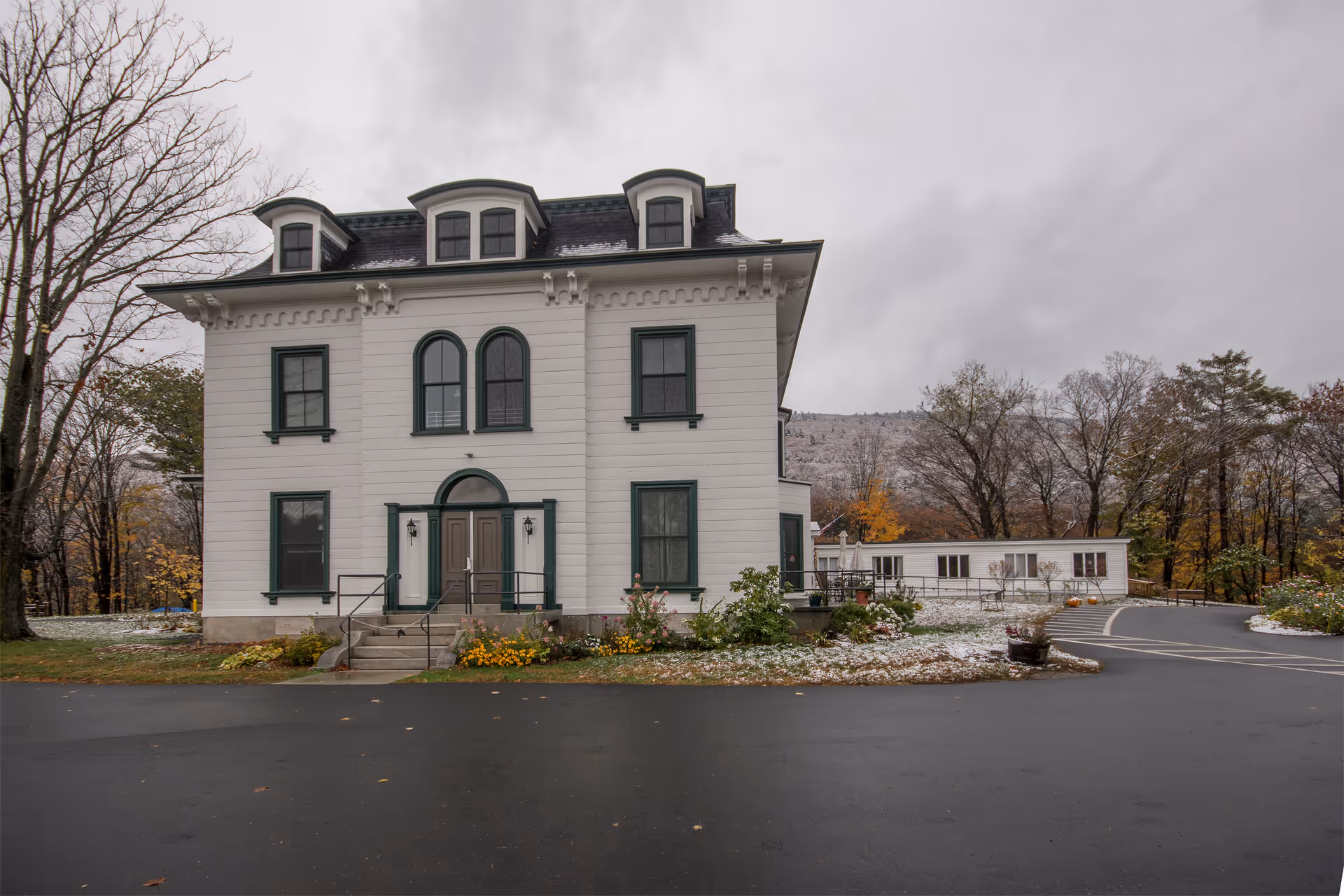A stately white multi-story building with dark green trim, front entrance, surrounded by trees.