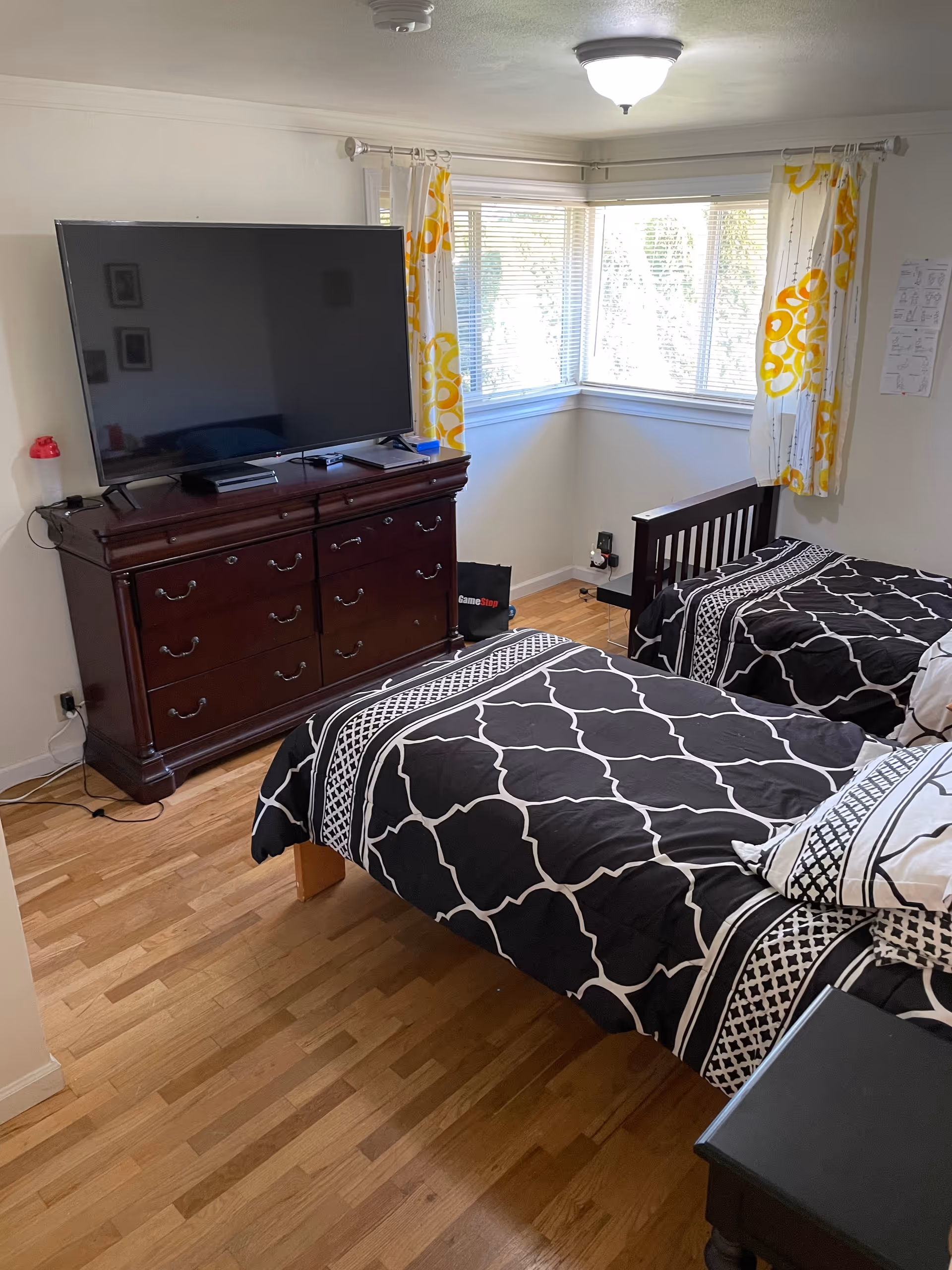 Two twin beds with black and white bedding, a dresser, and a large TV by windows.