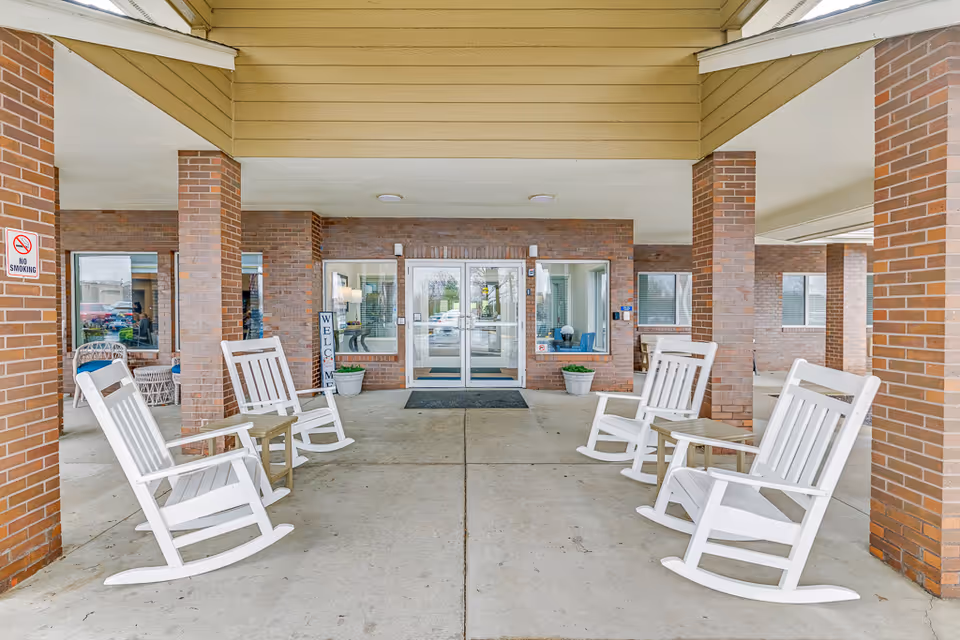 Entrance of Solstice Senior Living Joliet with white rocking chairs under a covered walkway.