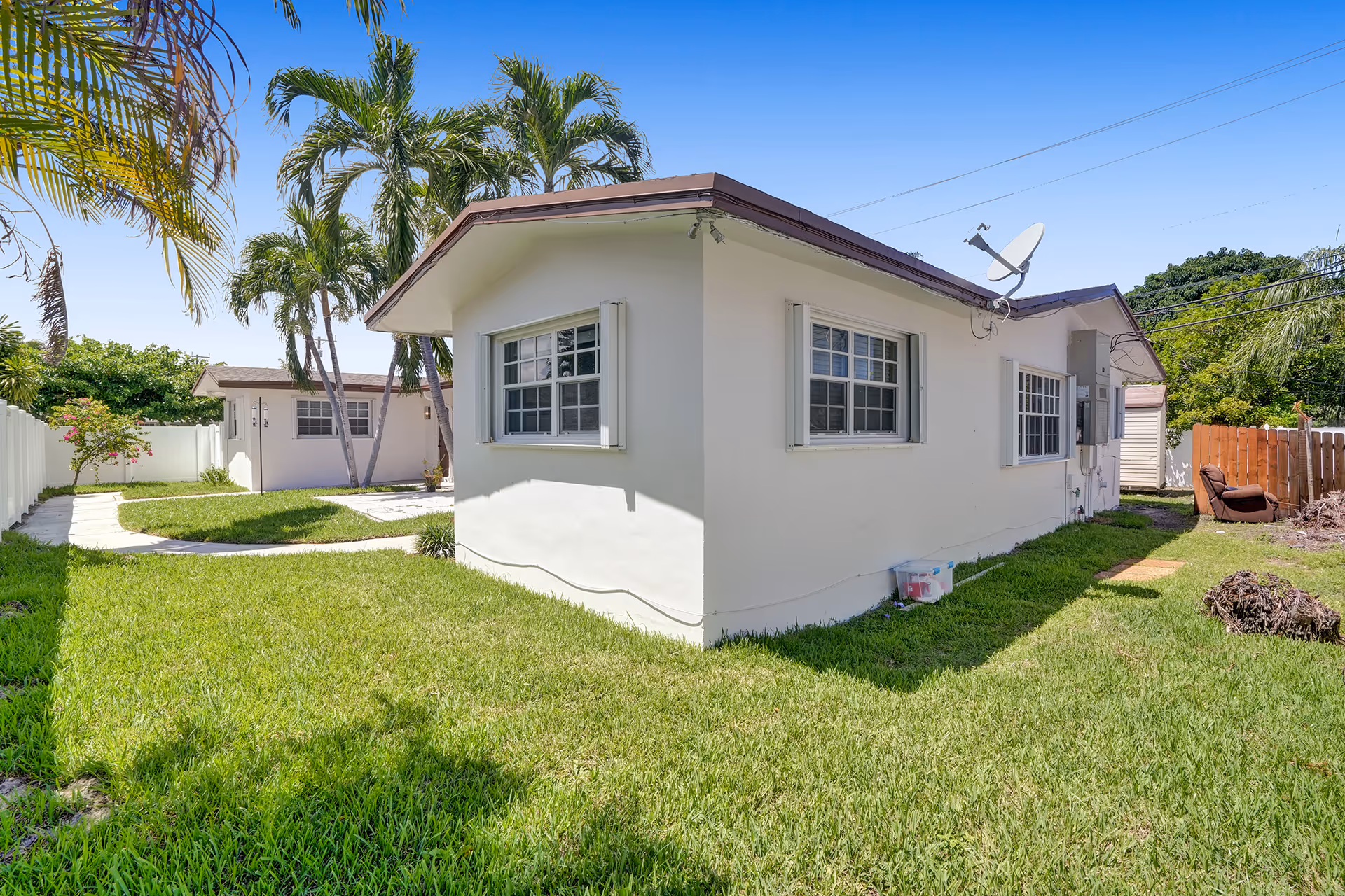 Single-story white building with windows, green lawn, and tall palm trees in the yard.