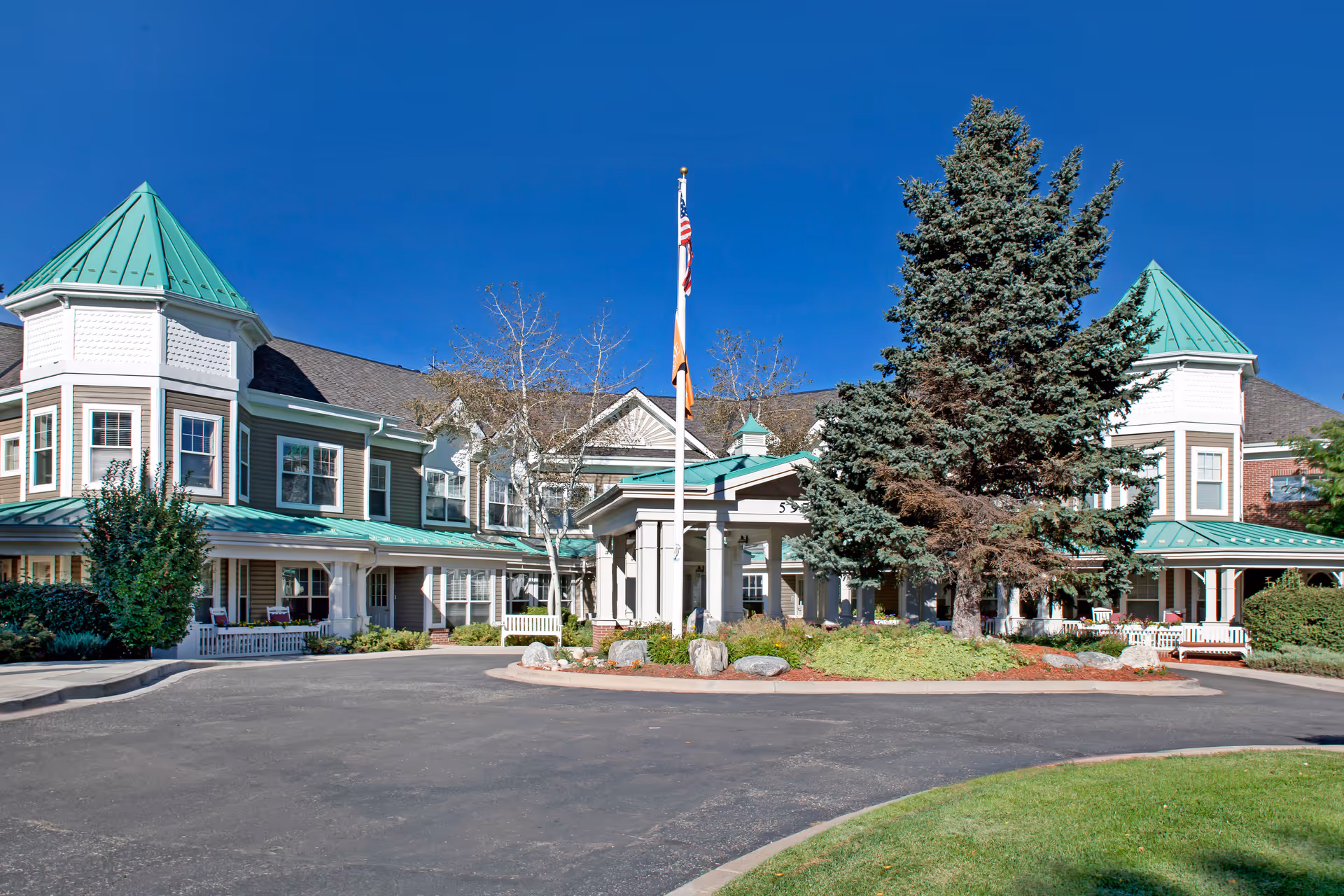 Exterior view of Sunrise at Orchard with green roofs, entrance, flagpole, and circular driveway.