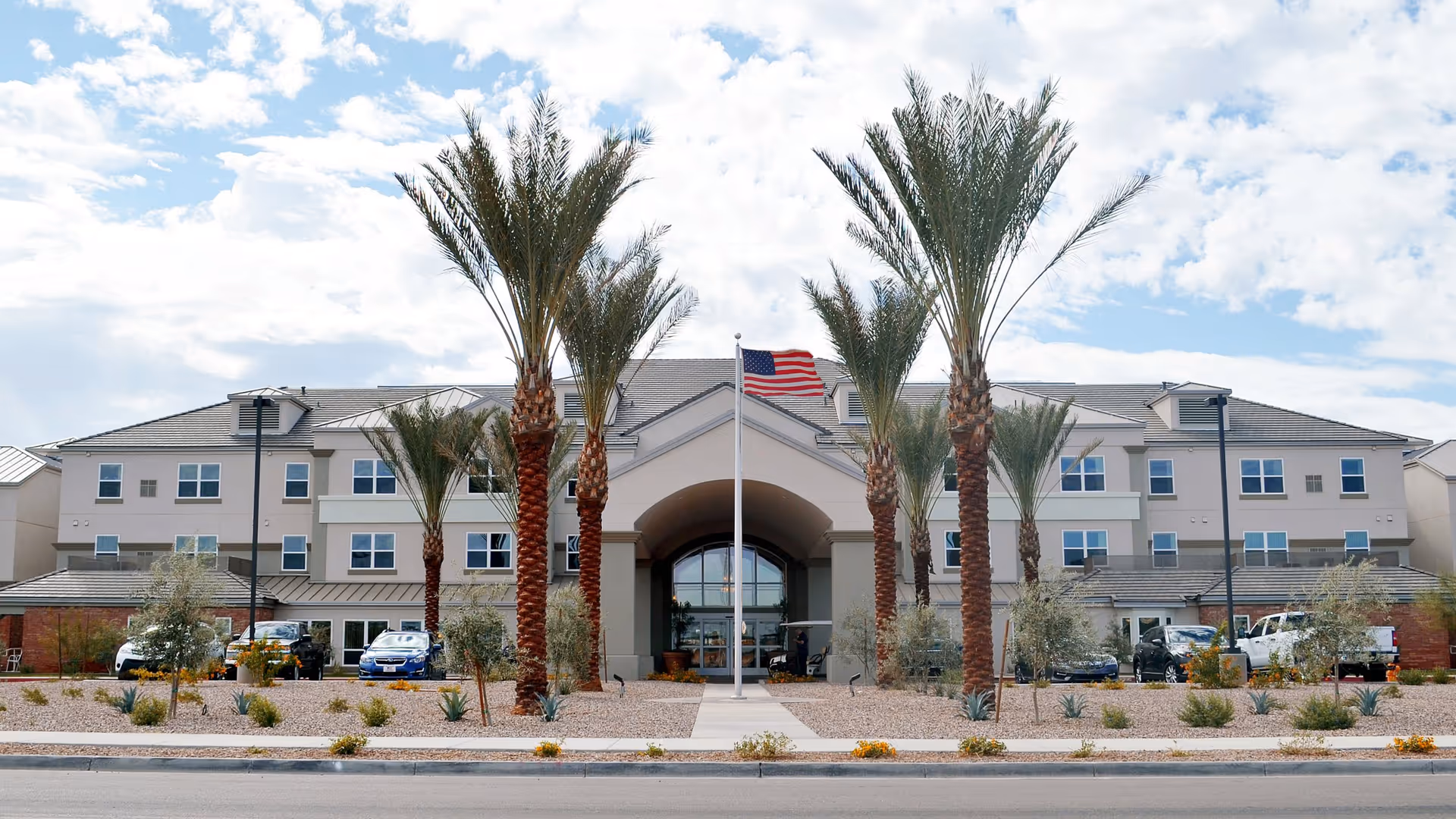 Exterior view of Copper Springs Retirement Community building with palm trees and an American flag