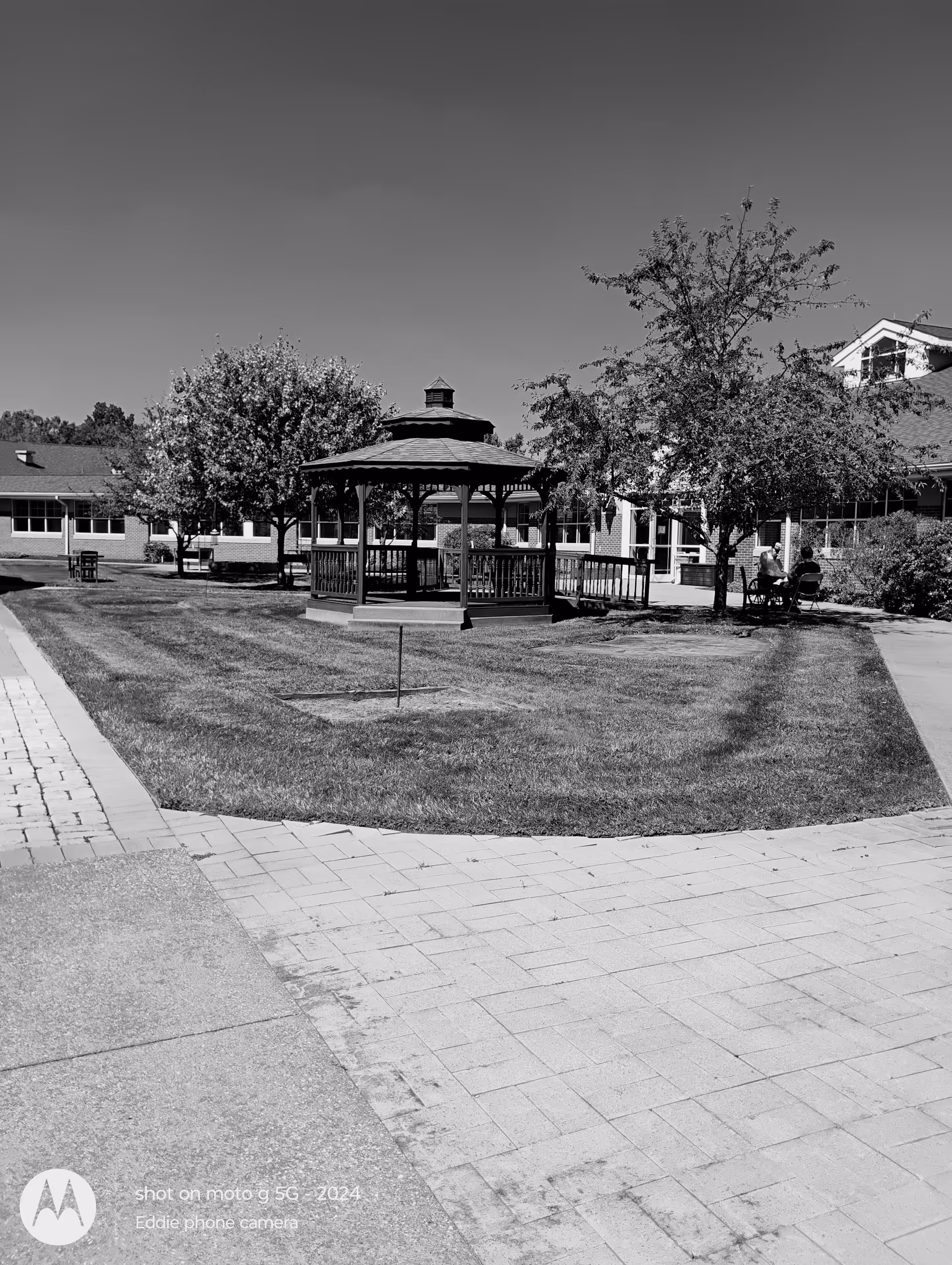 Outdoor courtyard with a gazebo, trees, and a building in the background.