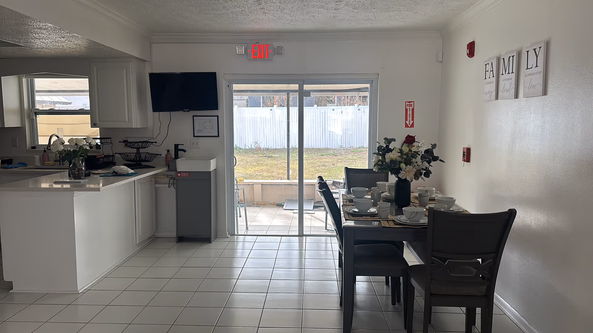 Dining area with a table set for a meal beside a kitchen, leading to a patio.