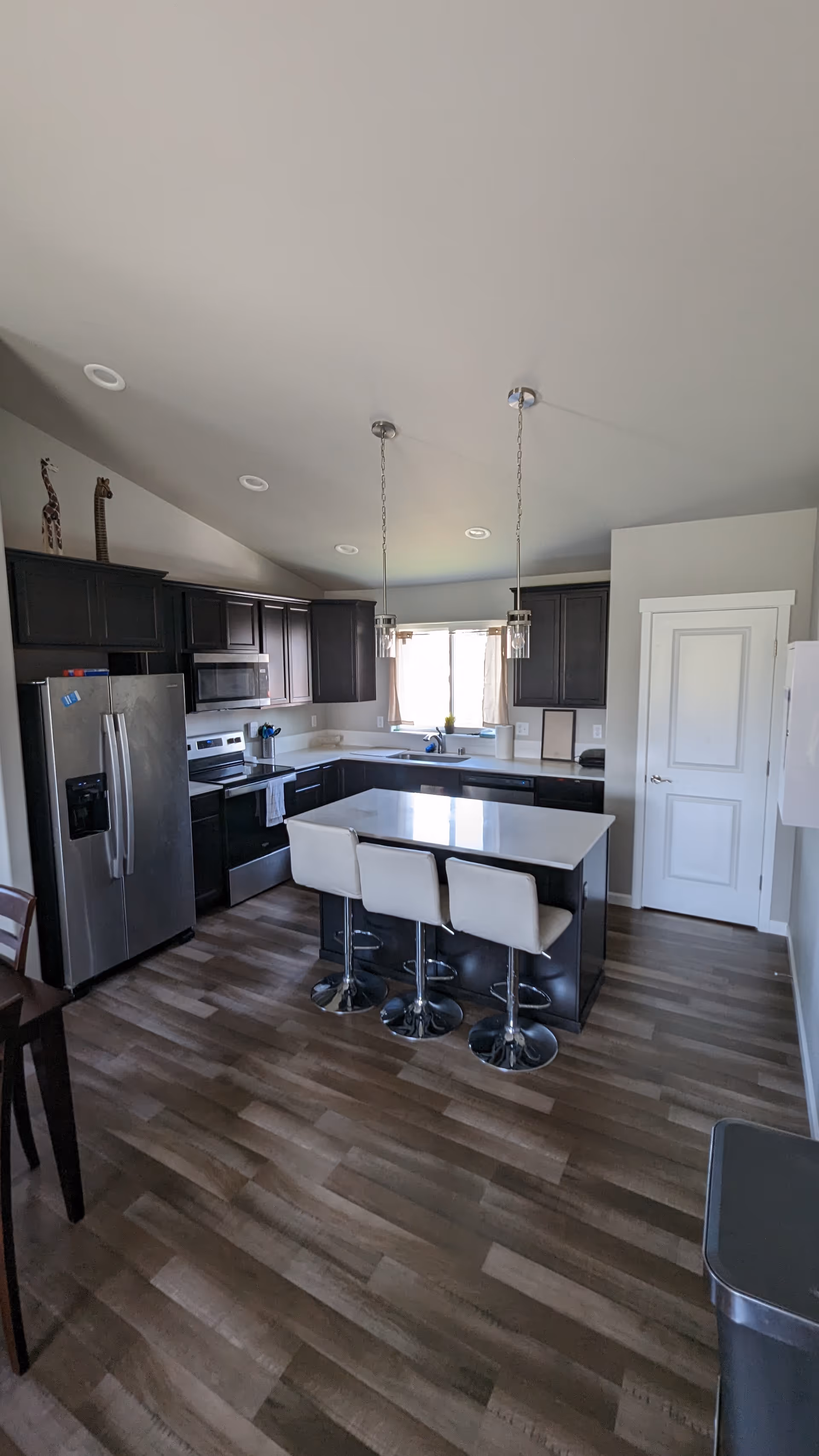 Modern kitchen with dark cabinets, stainless appliances, island, and white bar stools.