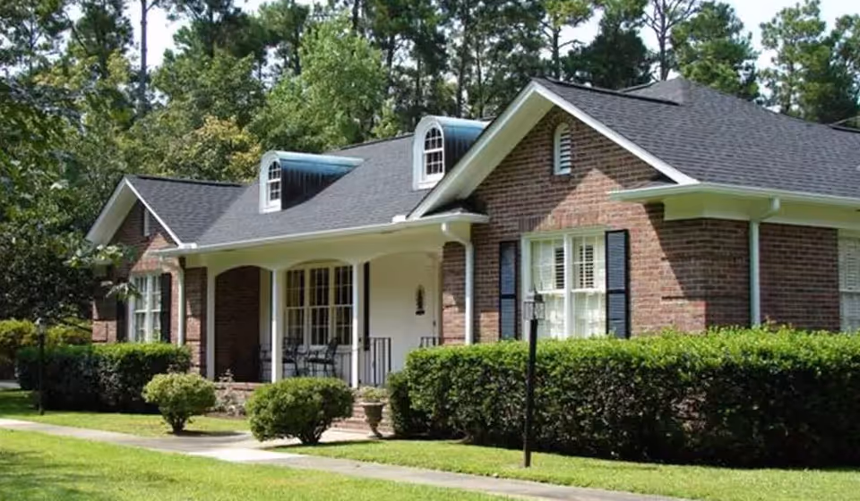 Front exterior of a single-story brick building with a covered porch, shrubs, and a well-kept lawn.