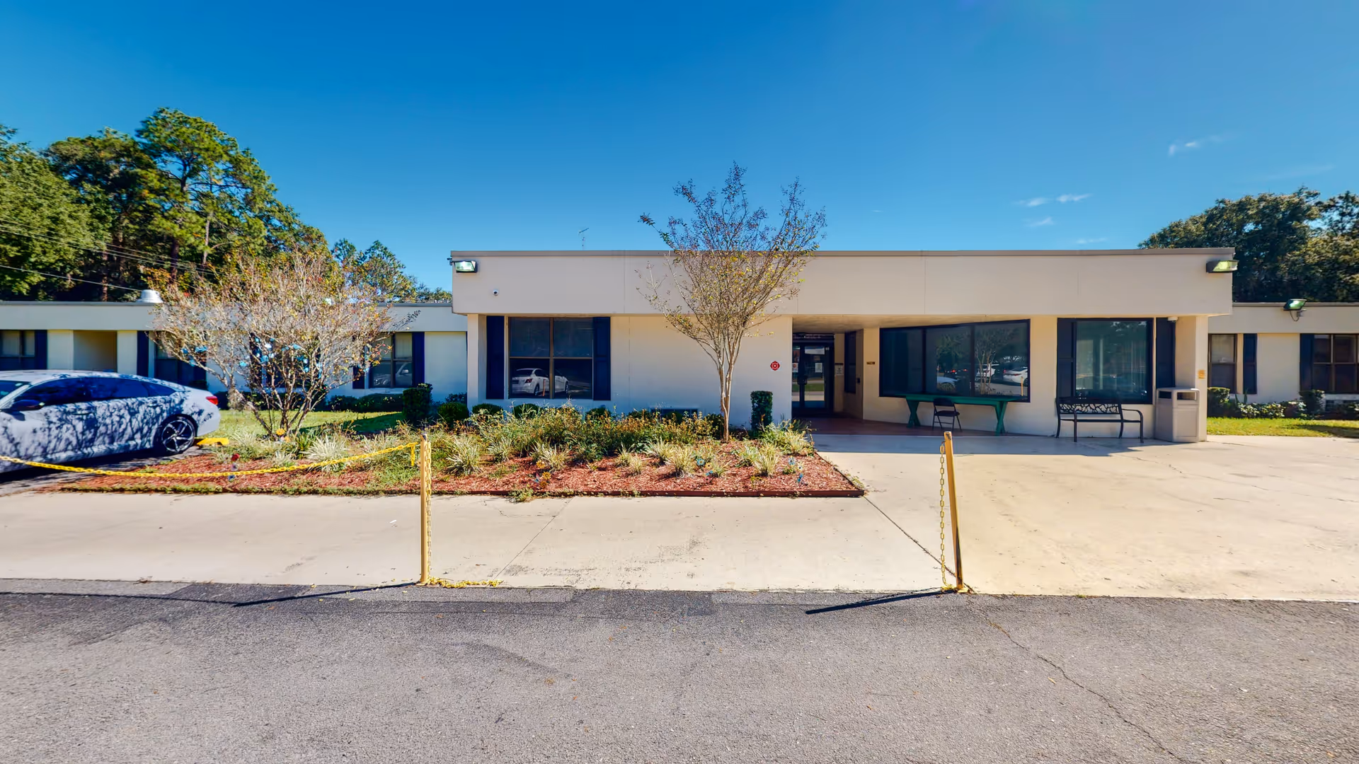 Single-story Riverwood Health and Rehabilitation Center exterior with entrance, windows, trees, and a parked car.
