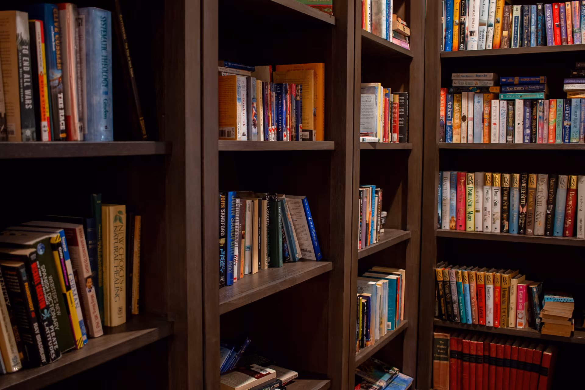 Interior view of dark wood bookshelves filled with colorful books along a hallway.