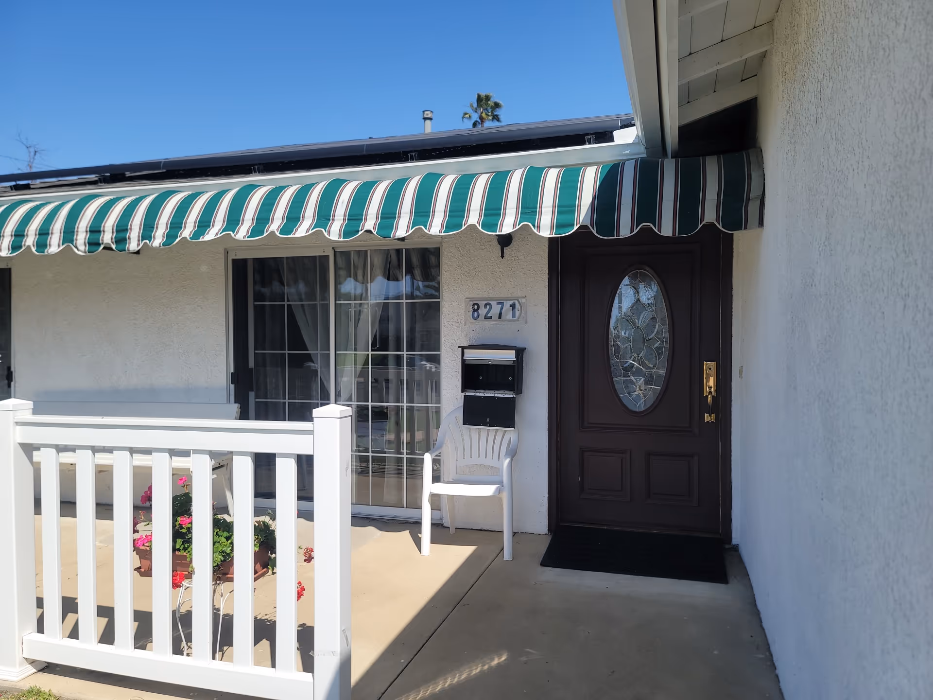 Front entrance of a building with striped awning, glass door, white railing, and chair.