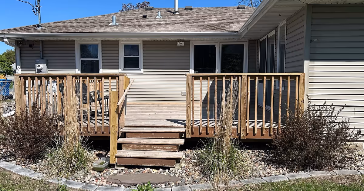 Back exterior view of a beige single-story building with a wooden deck and stairs.