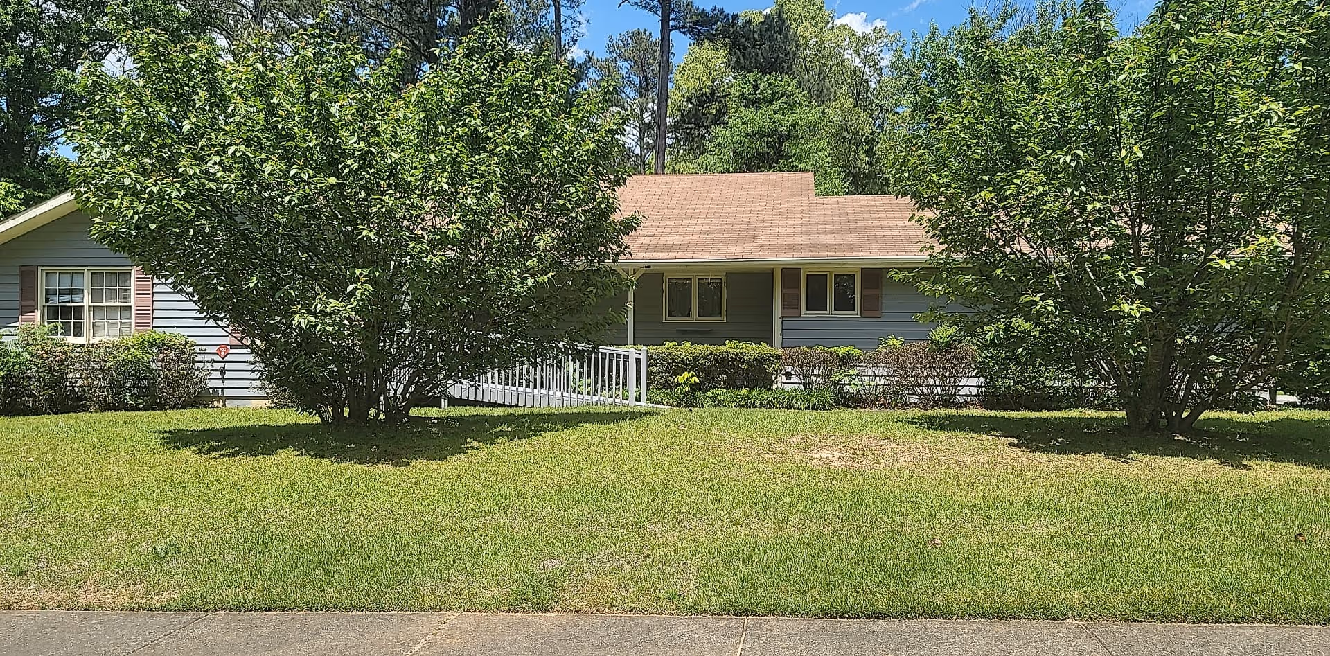 A single-story care home with a blue exterior, brown roof, and manicured front lawn.