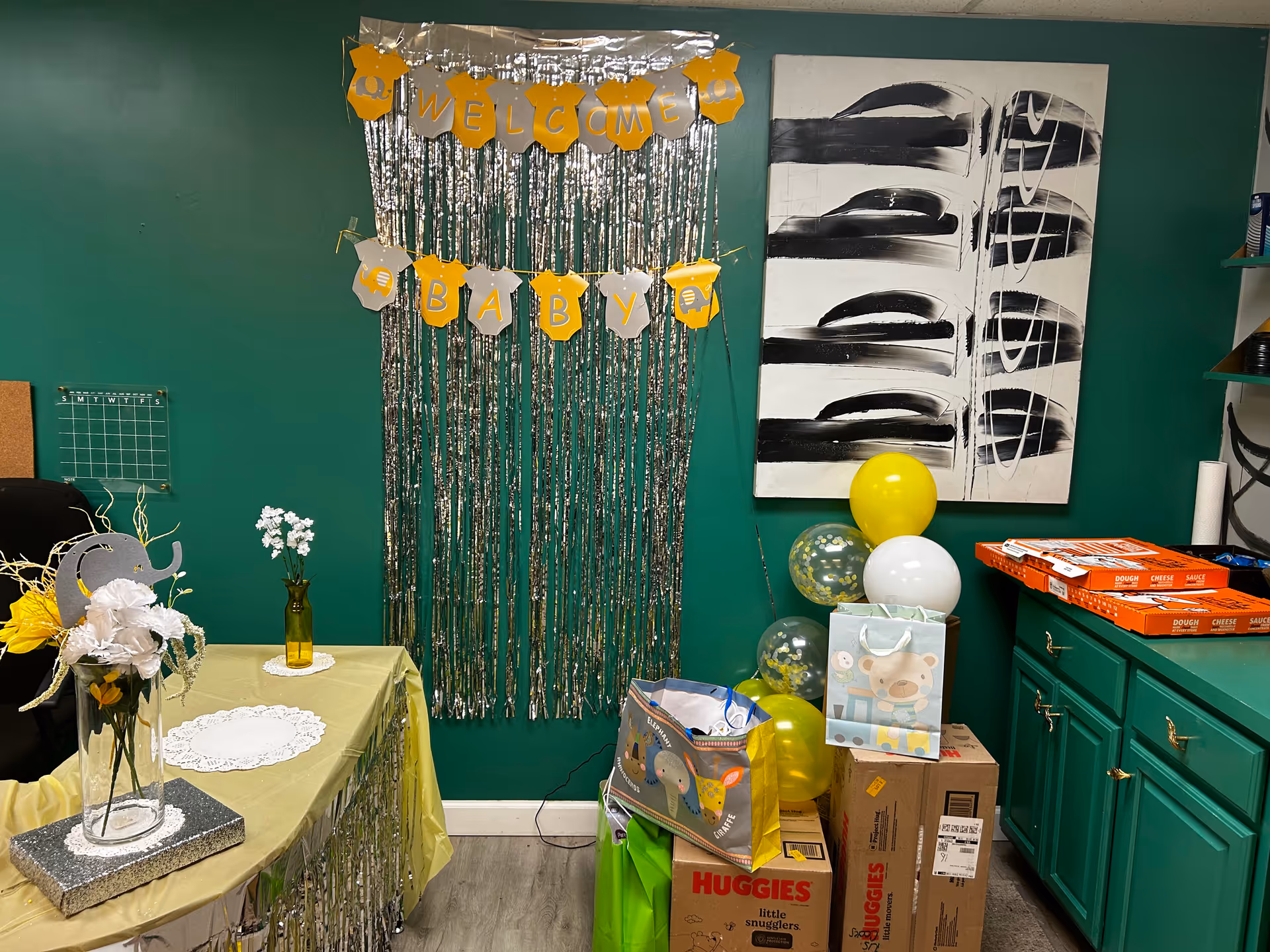 Interior room with green wall, Welcome Baby decorations, table setup, balloons, and gift boxes.