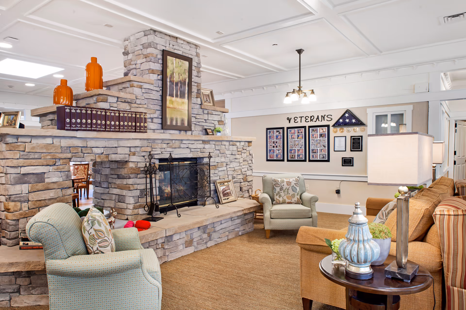 Sunlit living room with a stone fireplace, seating, and a veterans display wall.