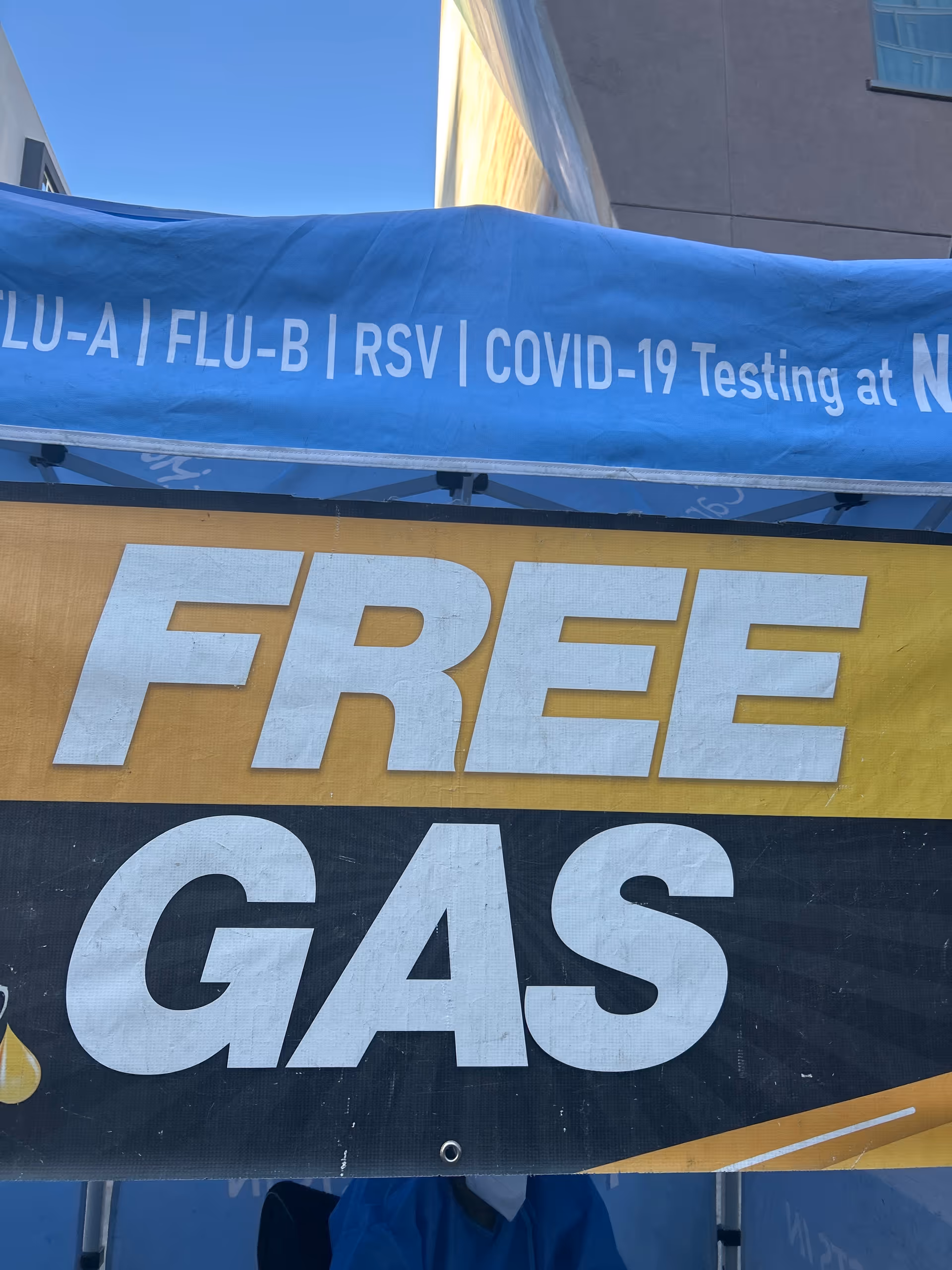 Outdoor blue canopy with a large yellow 'FREE GAS' banner and COVID testing text.