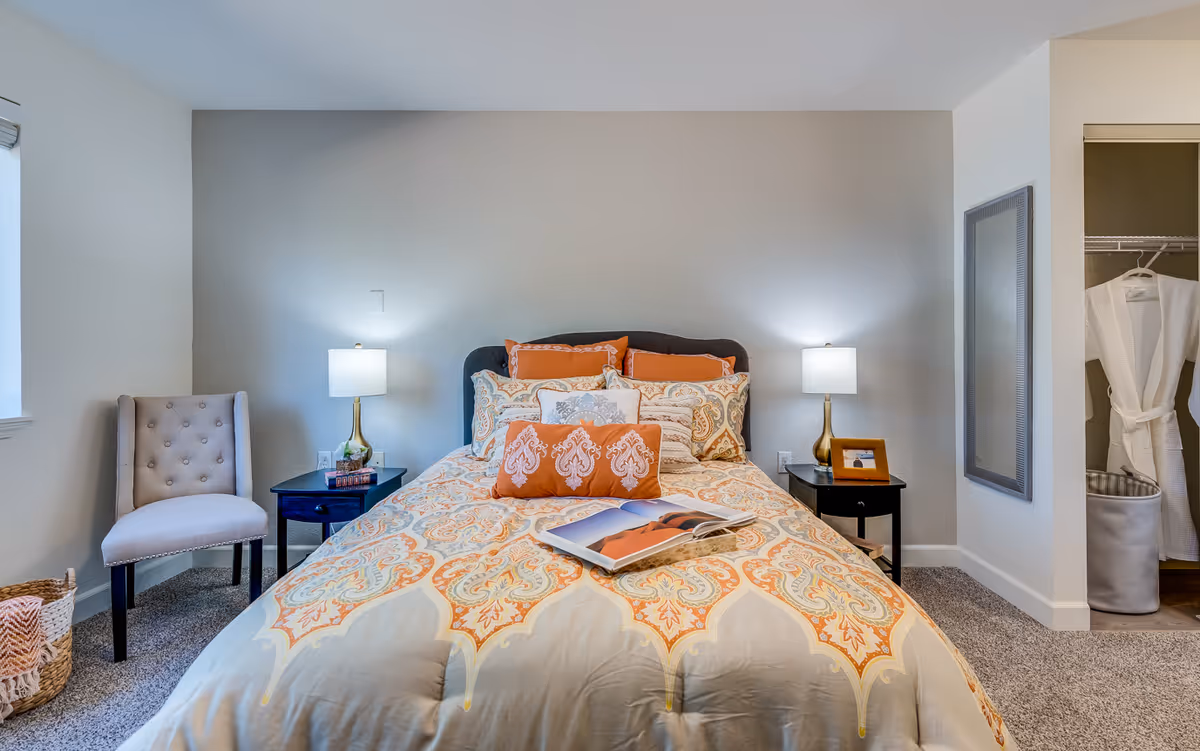 A neatly made bedroom with a patterned duvet, lamps, and a closet.