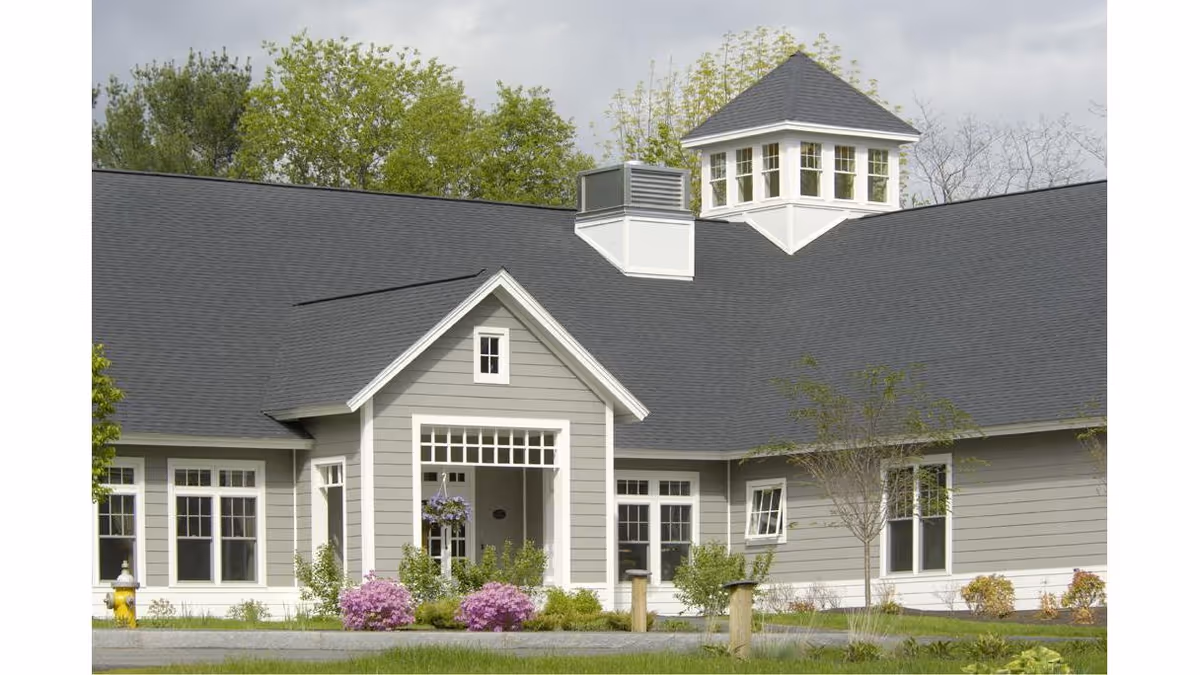 Gray, single-story senior living facility with a gabled entrance and manicured shrubs.