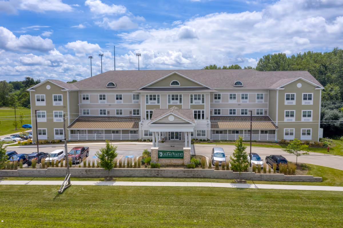 A three-story senior living building with a landscaped entrance and parked cars.