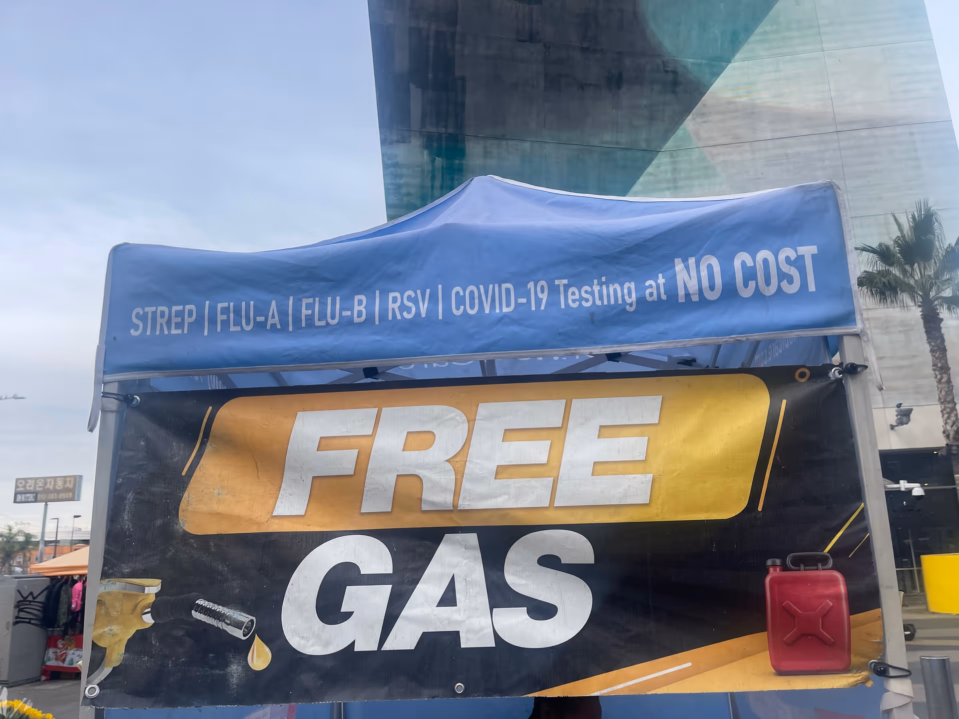 Blue tent advertising no-cost COVID-19 testing beside a 'FREE GAS' banner outdoors.