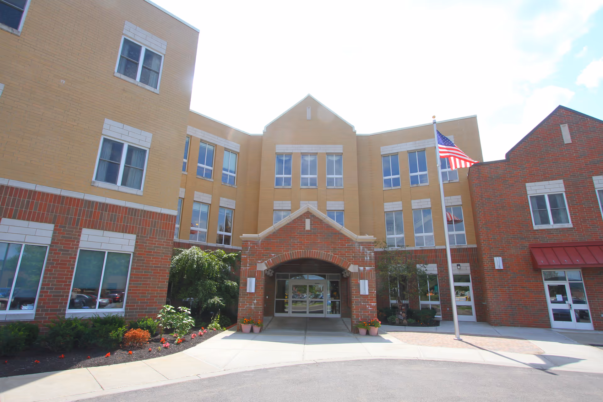 Front exterior of a multi-story senior living center with brick facade, entrance arch, and landscaping.
