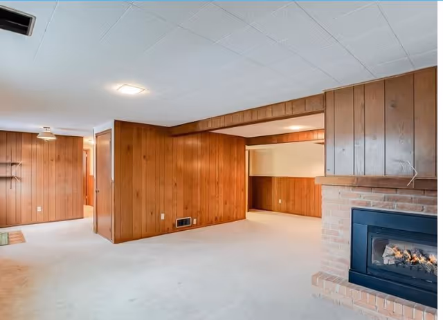 Interior wood-paneled living area with carpet, fireplace, and open doorway.