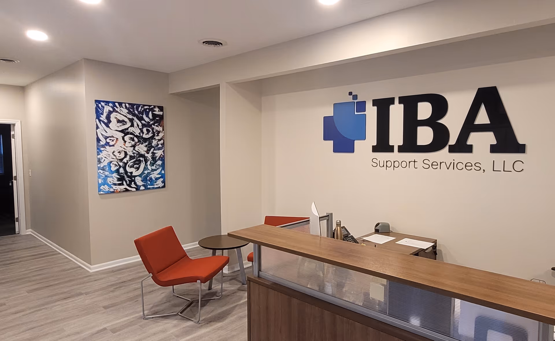 Reception area with a wooden counter, red chairs, and IBA Support Services logo.
