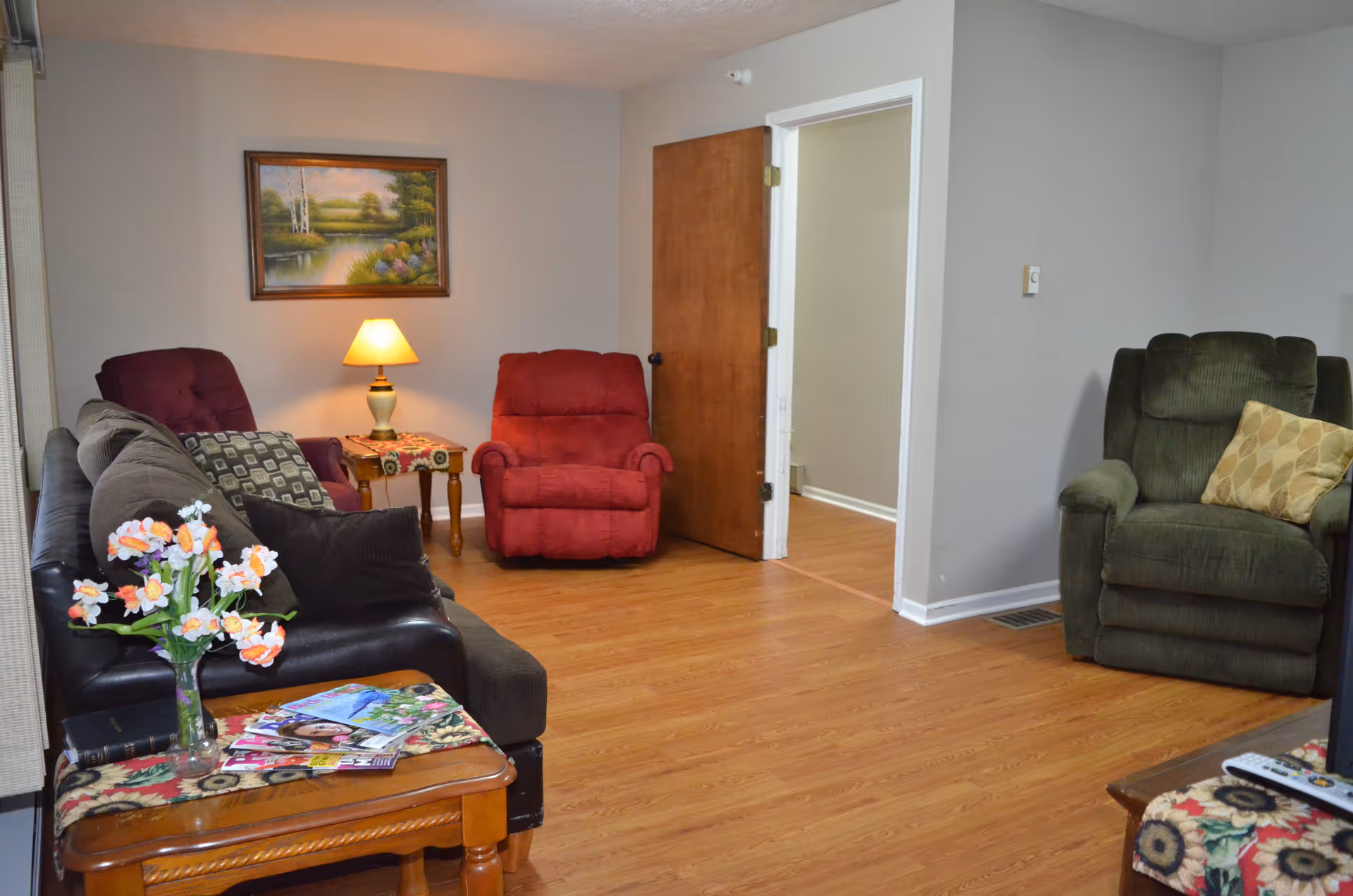 Cozy living room with sofa, recliners, lamp, and magazines.