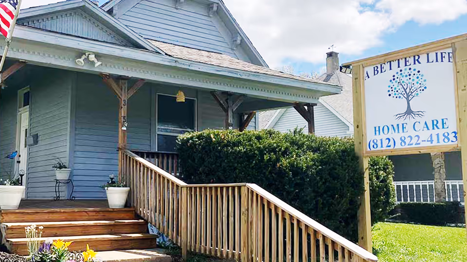 Blue single-story home care facility exterior with porch steps and a sign reading A Better Life.