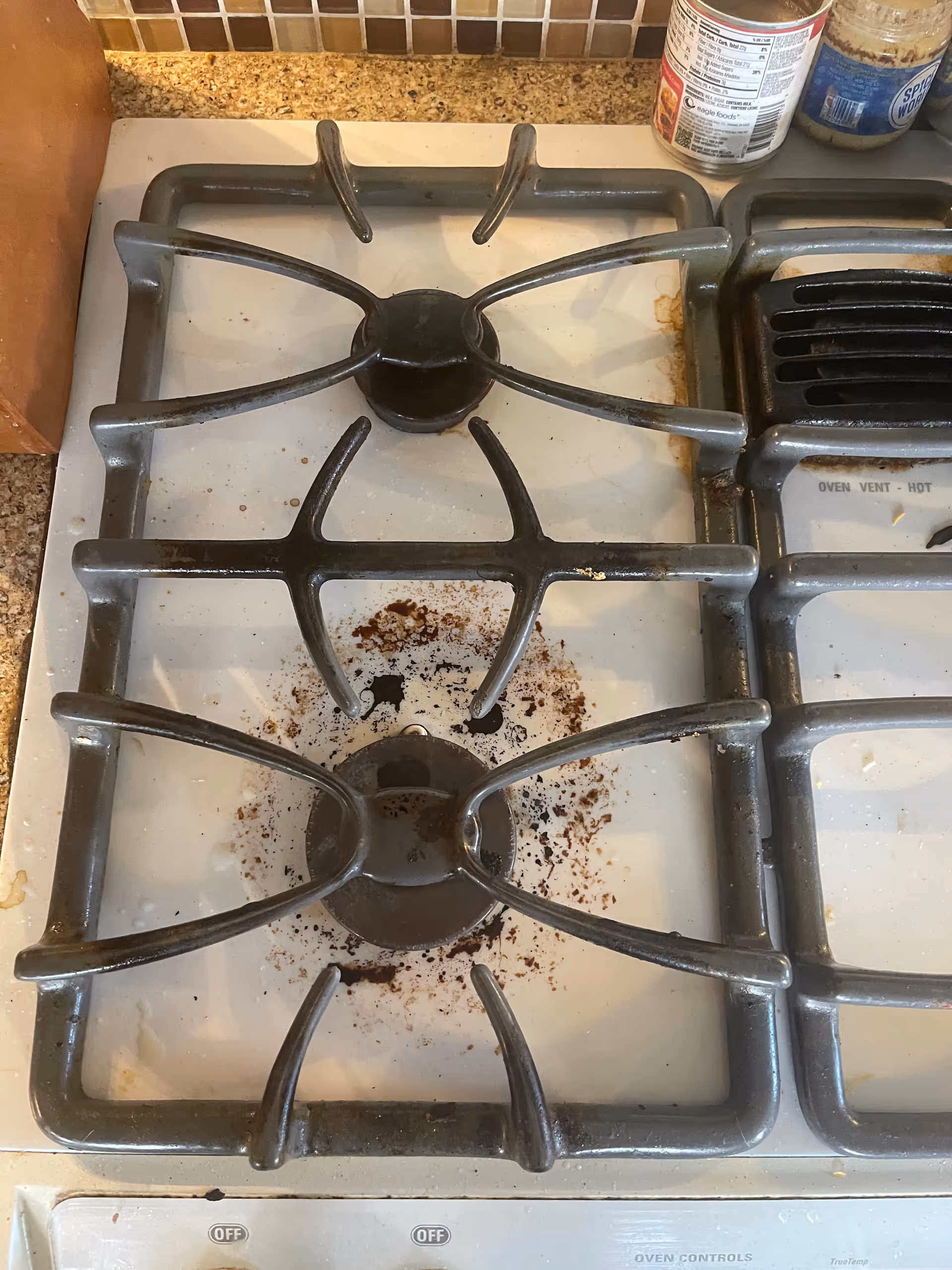 Close-up view of a dirty gas stove with four burners and stains.