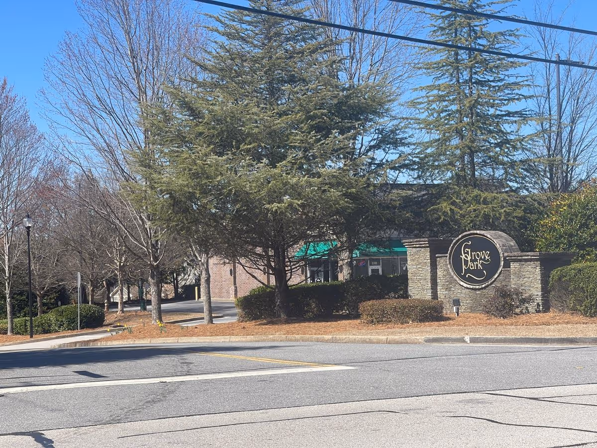 Entrance sign reading 'Grove Park' beside trees and a low brick building viewed from the street.