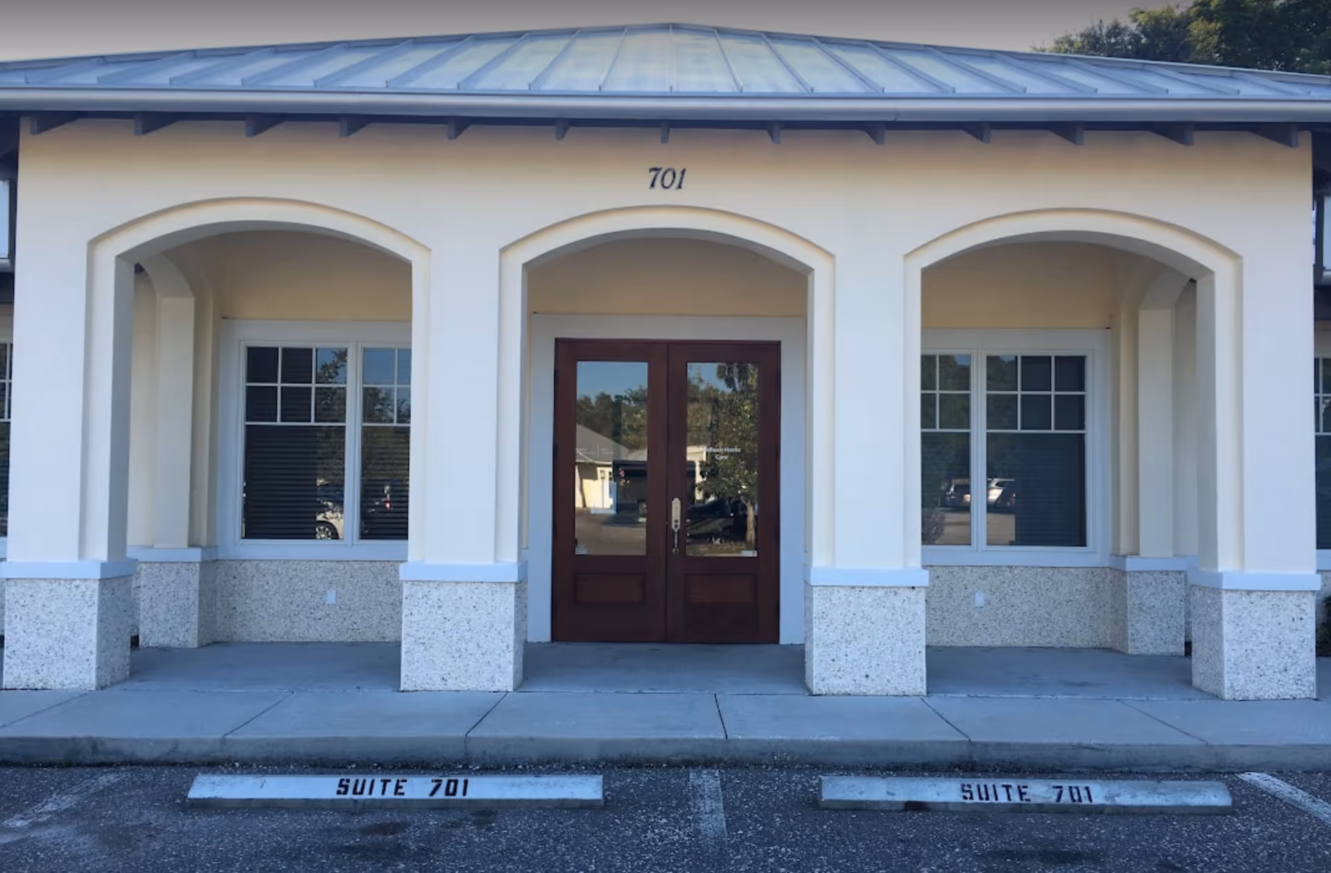 Cream-colored senior living facility exterior with arched entryways and a central wooden double door.