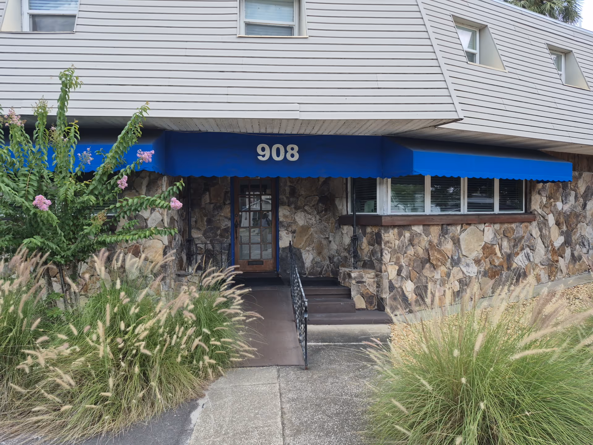Exterior of a stone-faced senior building with blue awning and 908.