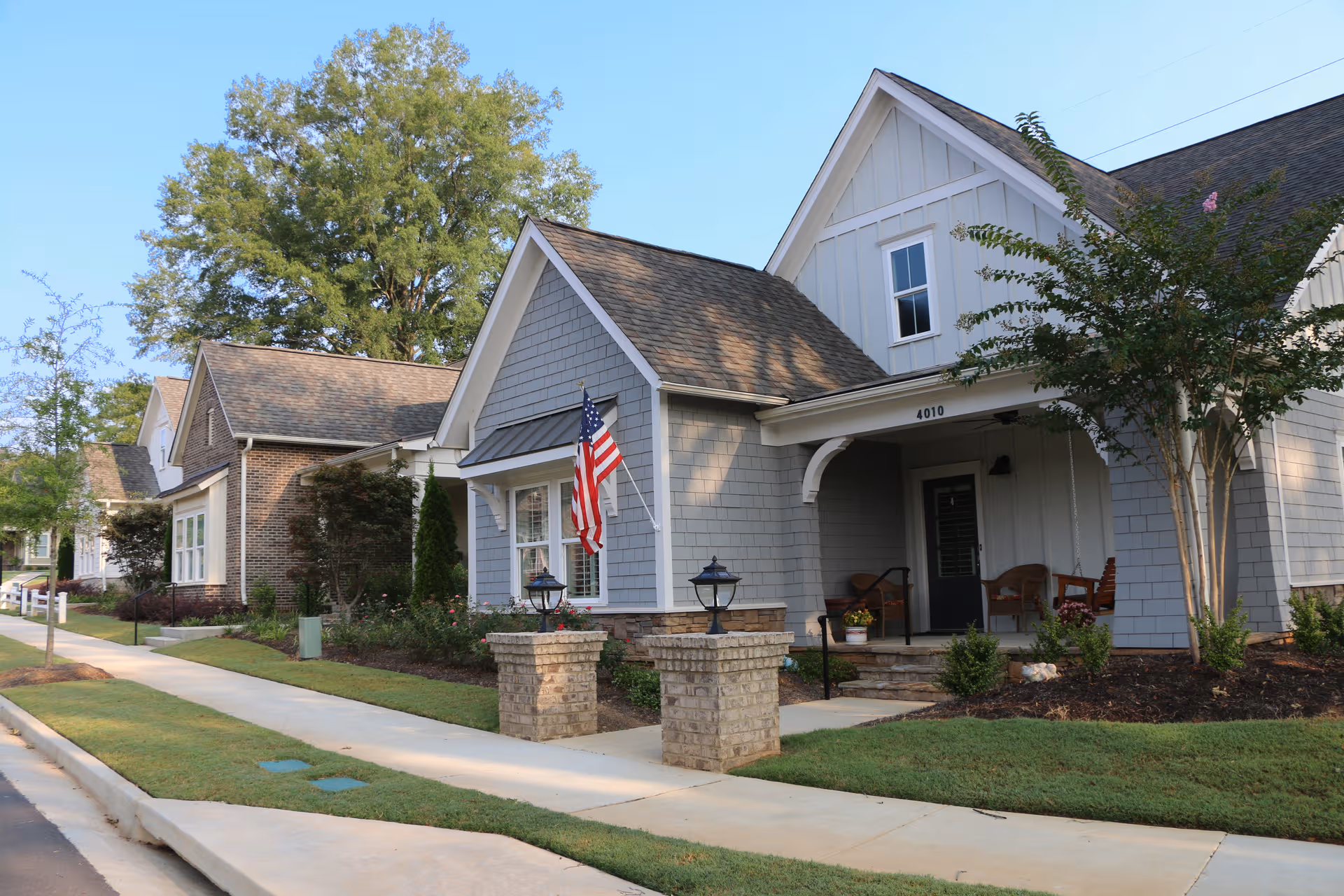 Row of pastel senior living homes with porches, flag, and a manicured lawn along a sidewalk.