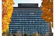 Tall glass-front senior living building labeled Holladay Park Plaza, framed by orange autumn trees.