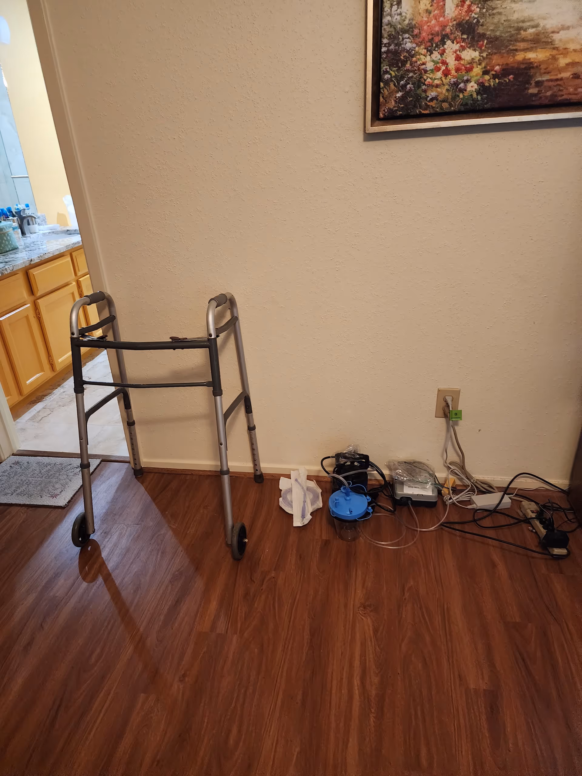 A walker stands in a sparsely furnished interior hallway near a kitchen area with cords.