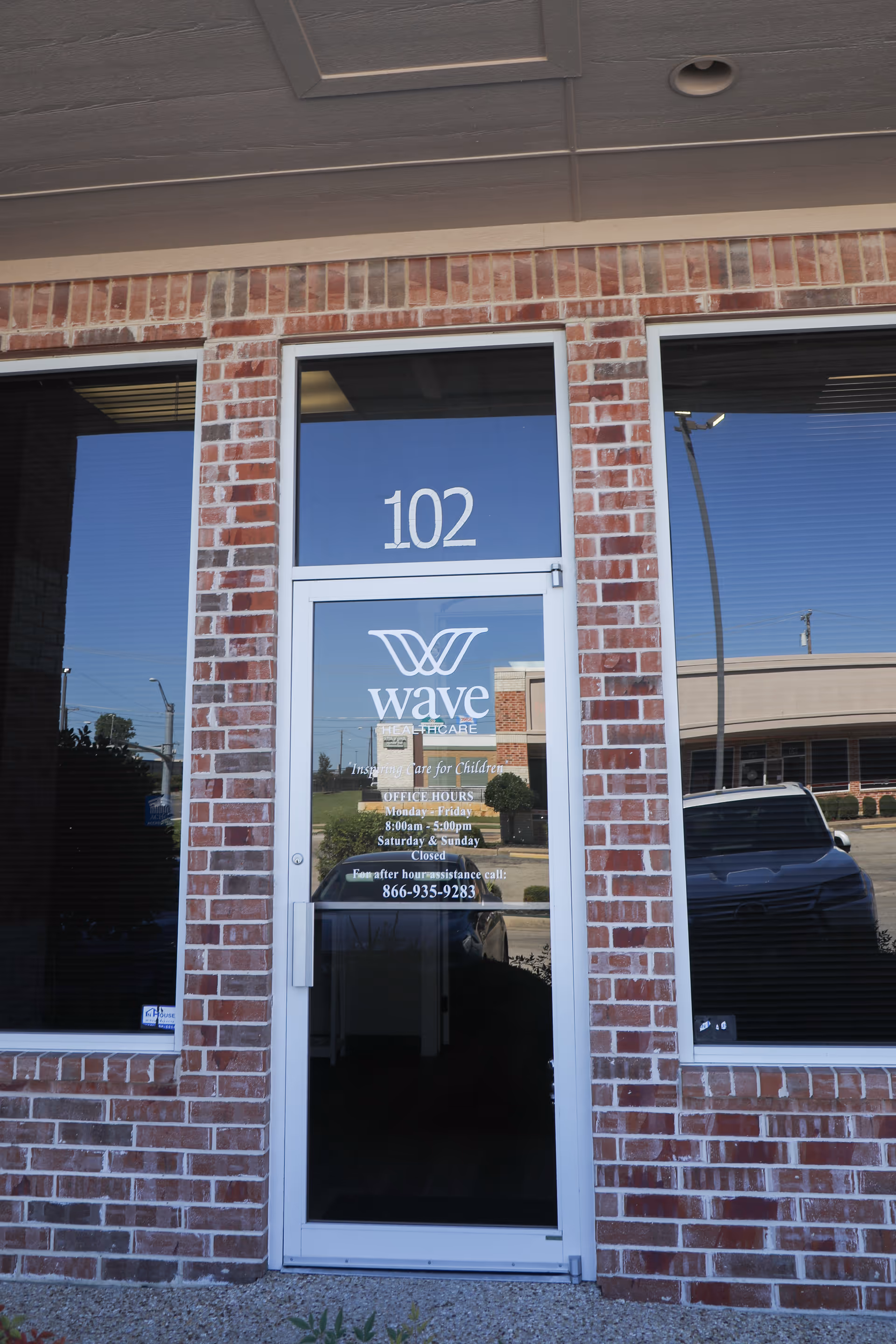 Brick storefront entrance with door labeled Wave Healthcare, 102 above, street reflection.