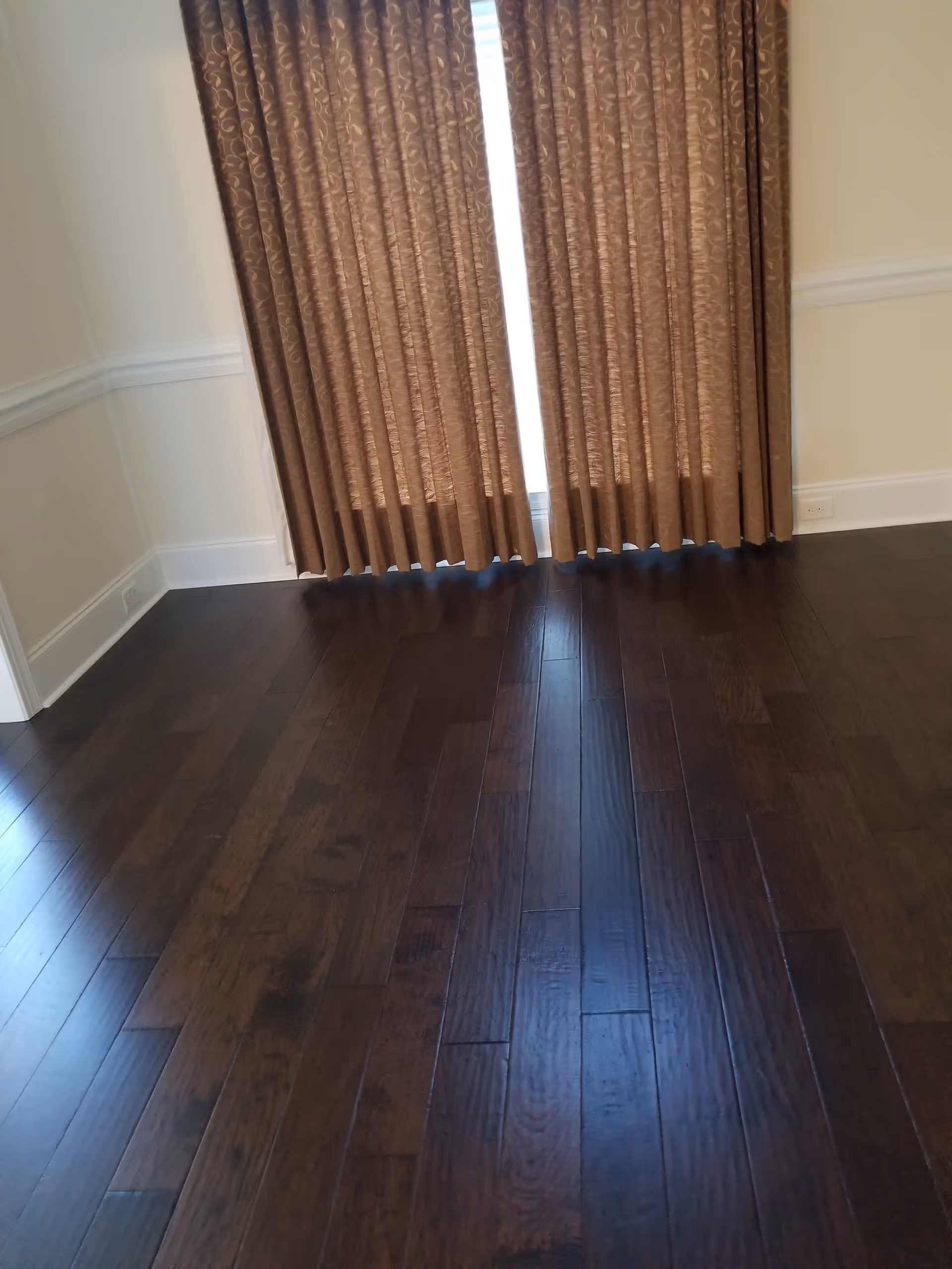 Dark wooden floor with brown curtains covering a window in an empty room