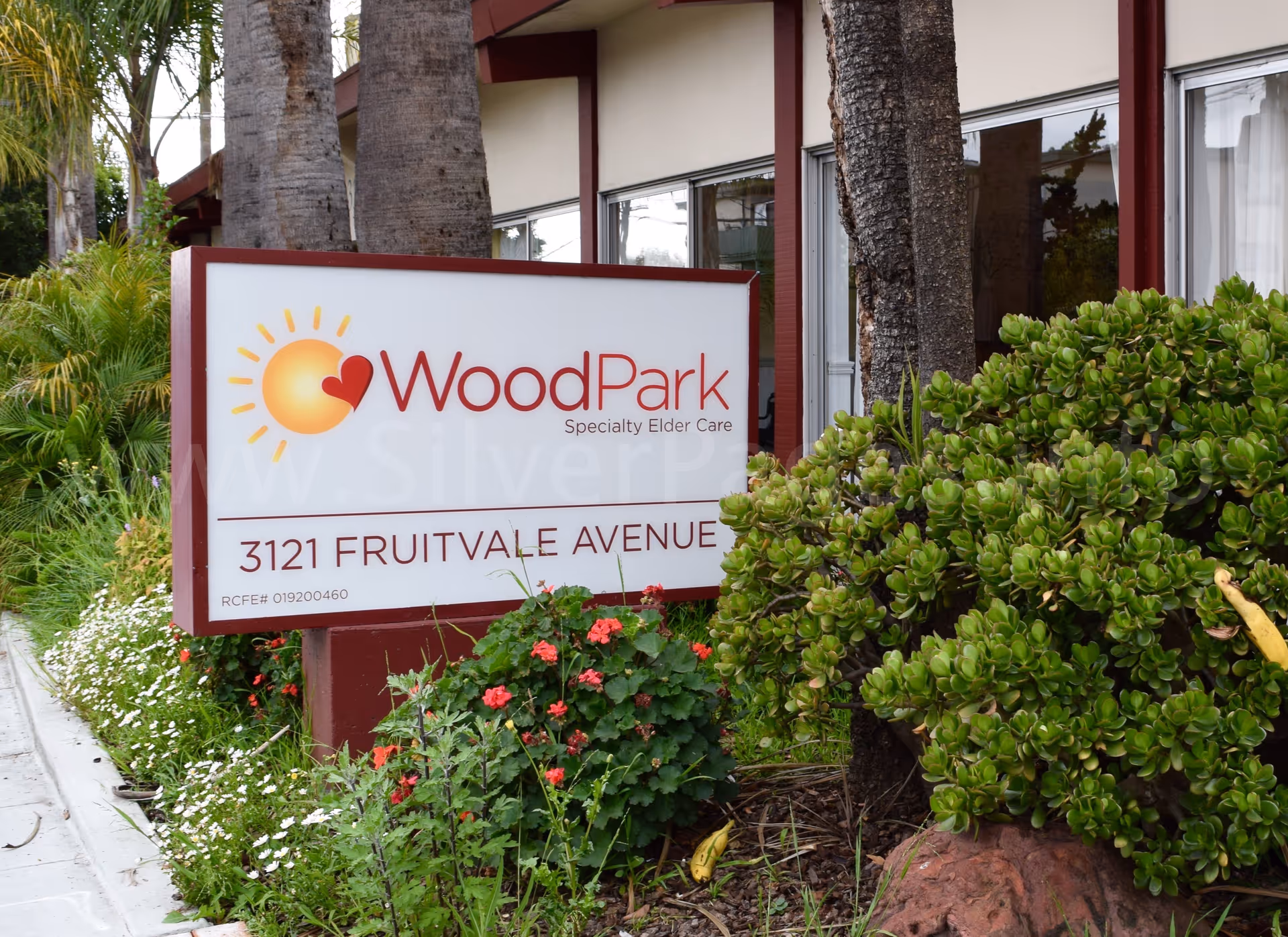 Exterior view of WoodPark elder care sign with greenery in front of building.
