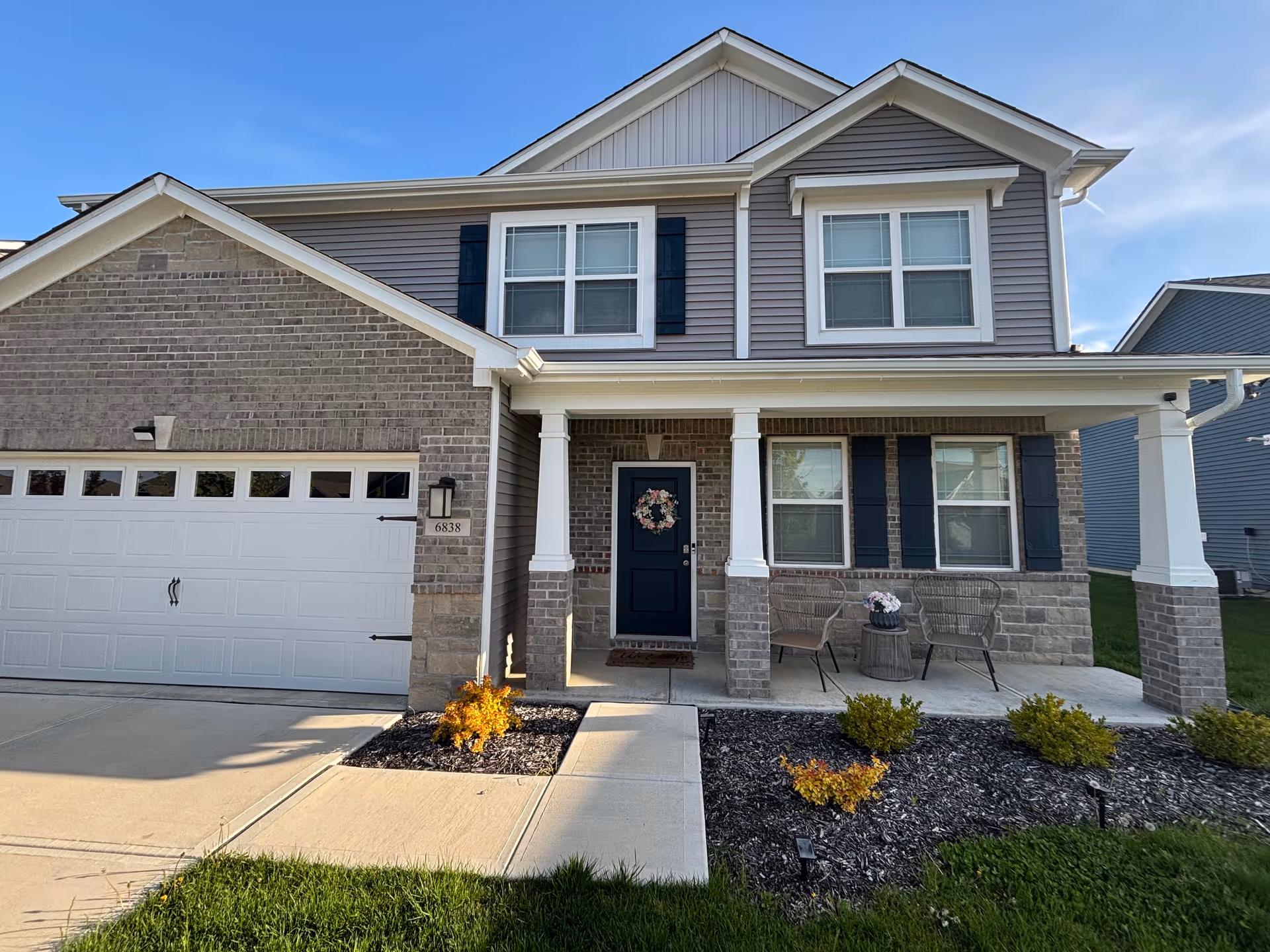 Two-story suburban house exterior with front porch, wreath on door, and a two-car garage.