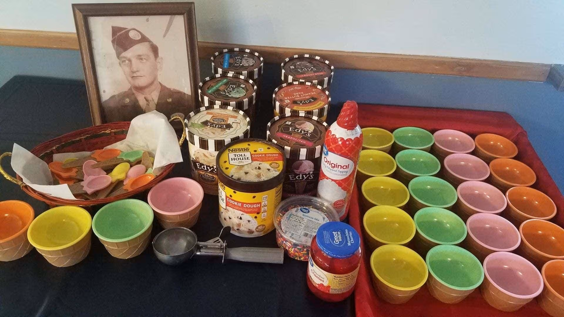 Colorful dessert cups and jars arranged on a table beside framed military photo in a facility.