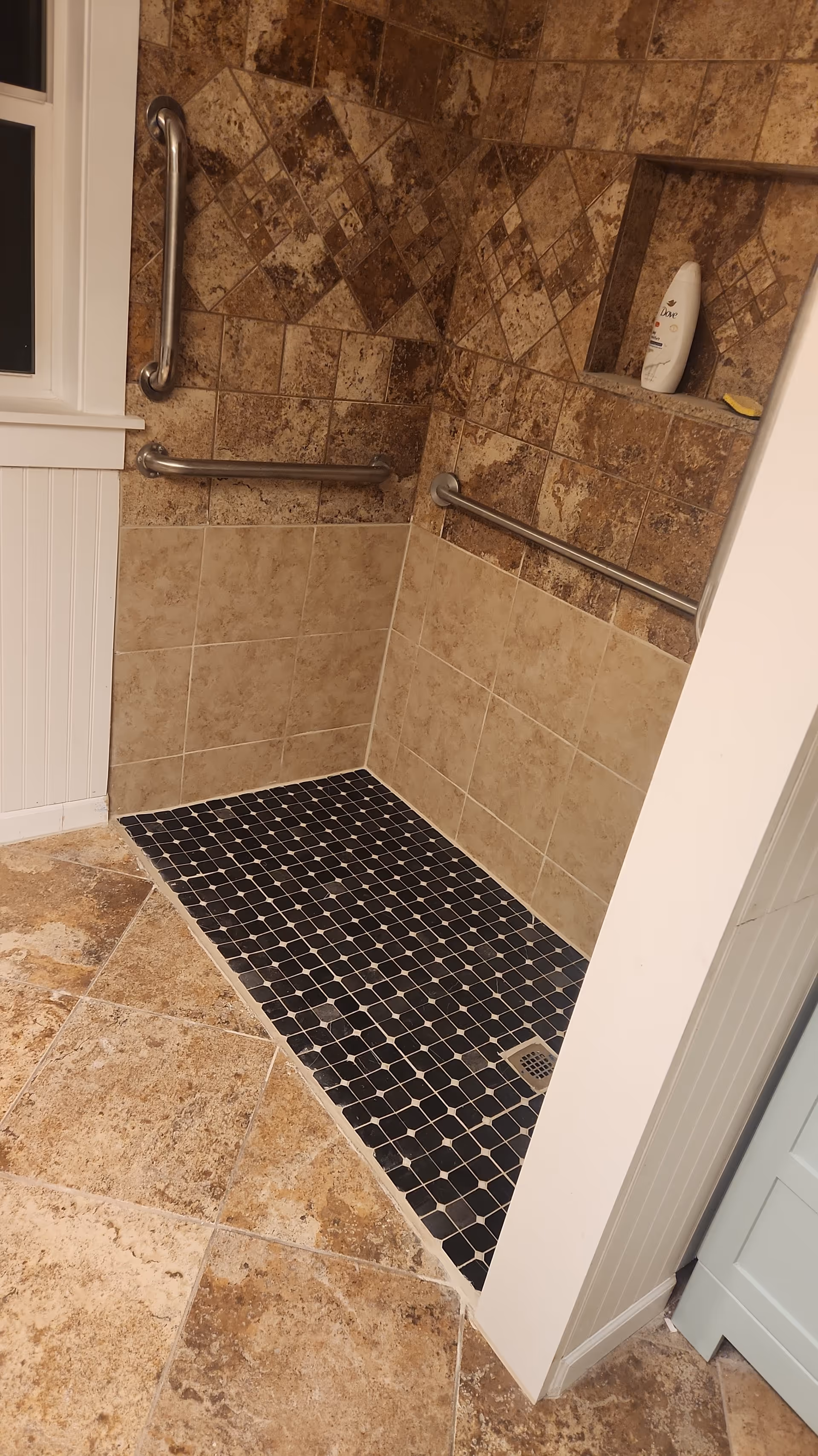 Wheelchair-accessible shower with grab bars, dark mosaic floor tiles, and a built-in niche.