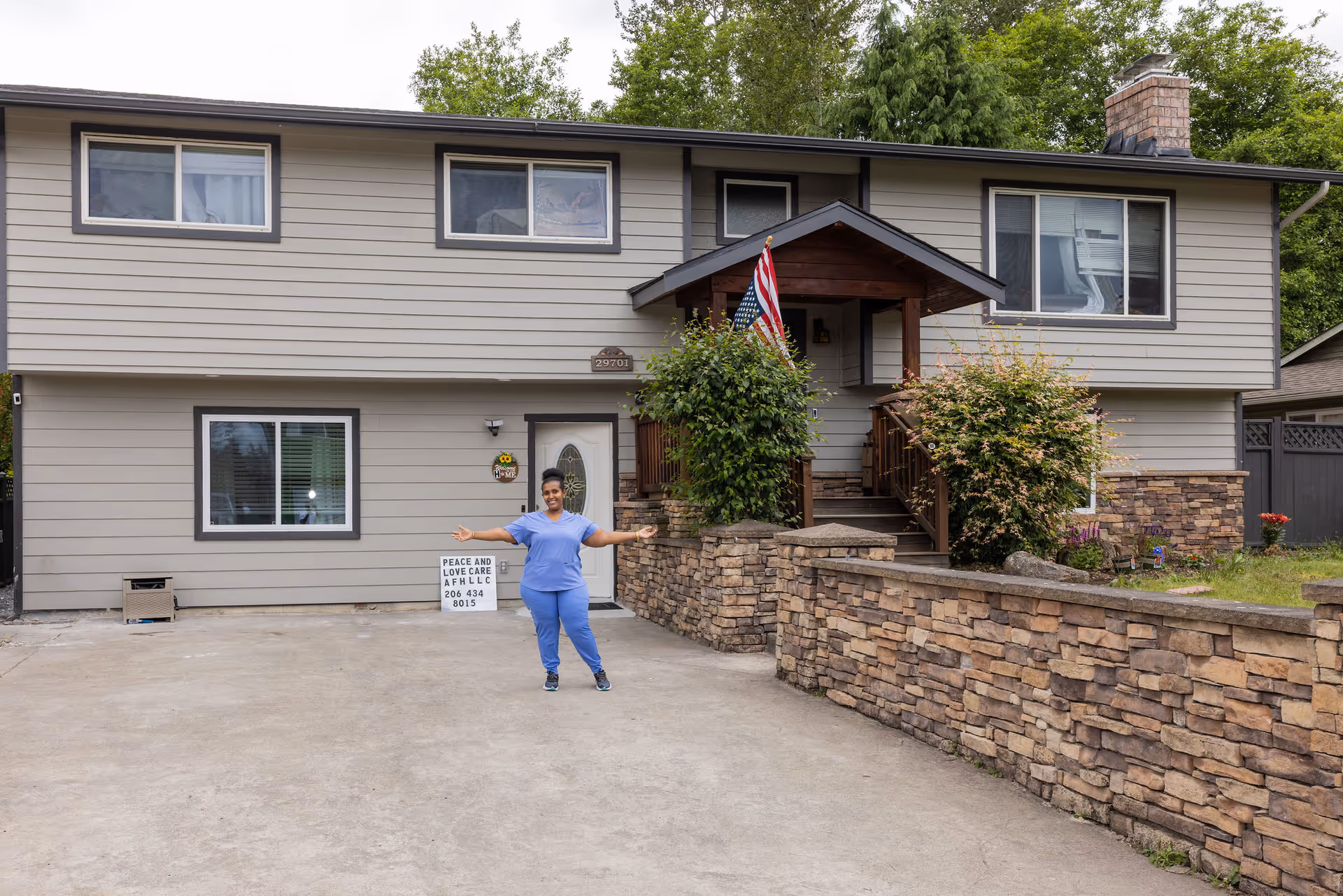 A person stands in the driveway of a two-story care home with stone wall and flag.