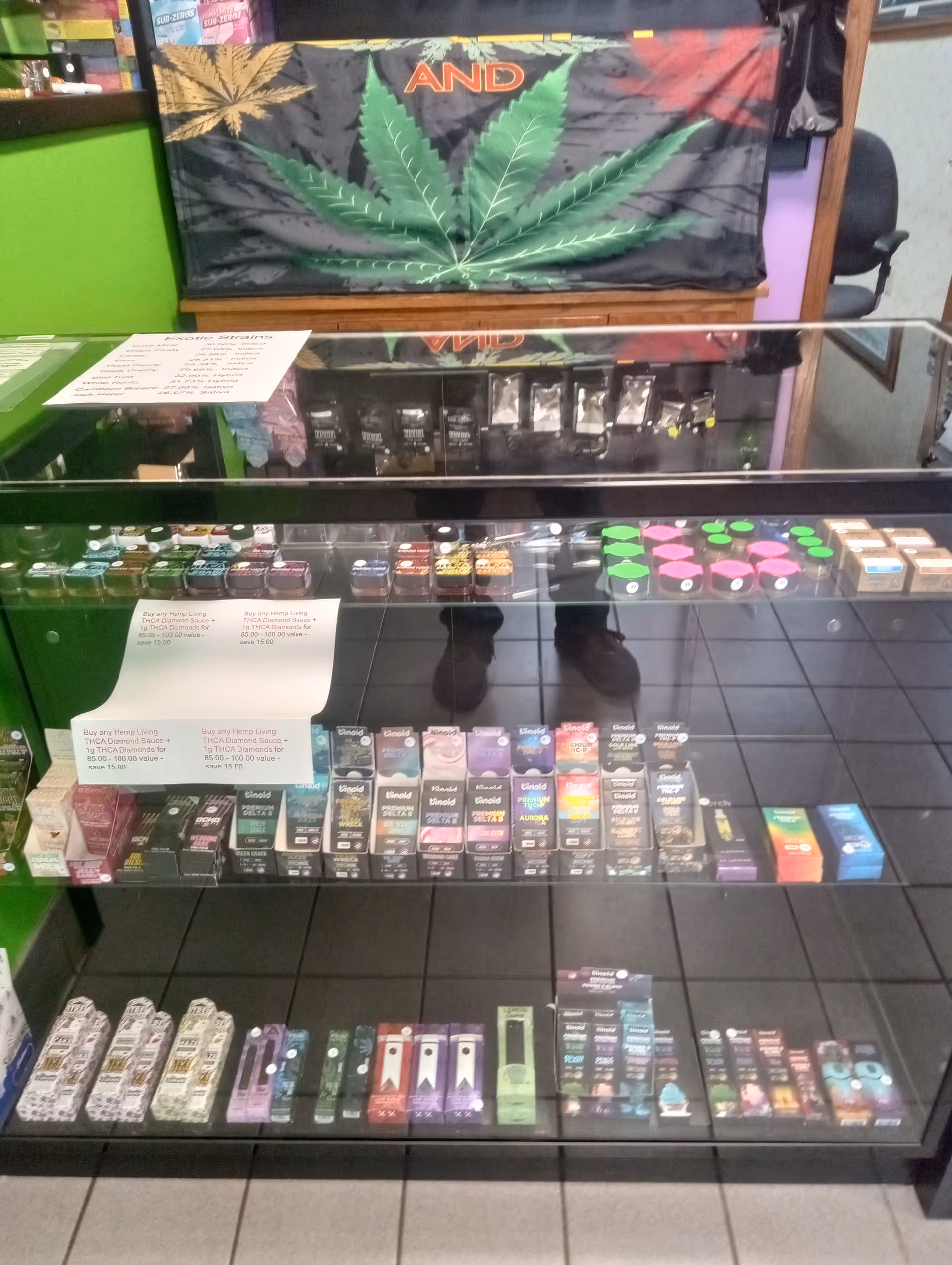 Glass display case with cannabis products and a large marijuana leaf banner behind.