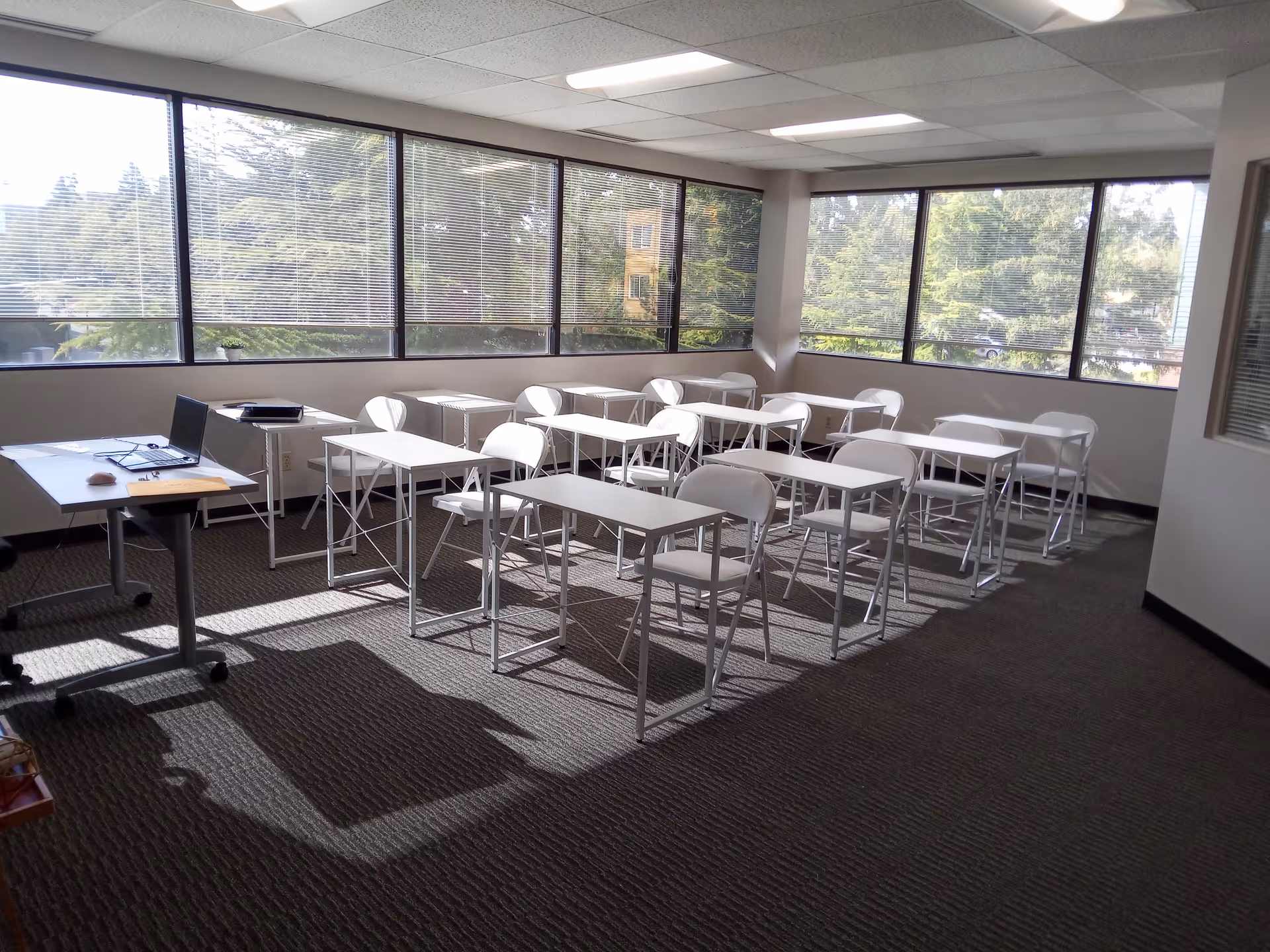 Bright training room with white desks and chairs arranged in rows by large windows.