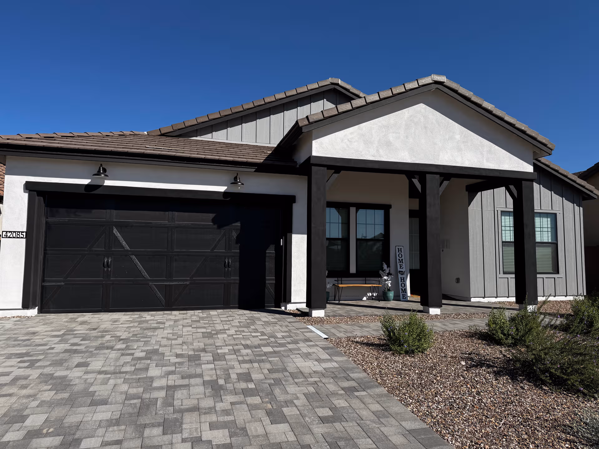 Modern single story house with a double garage, front porch, and desert landscaping.