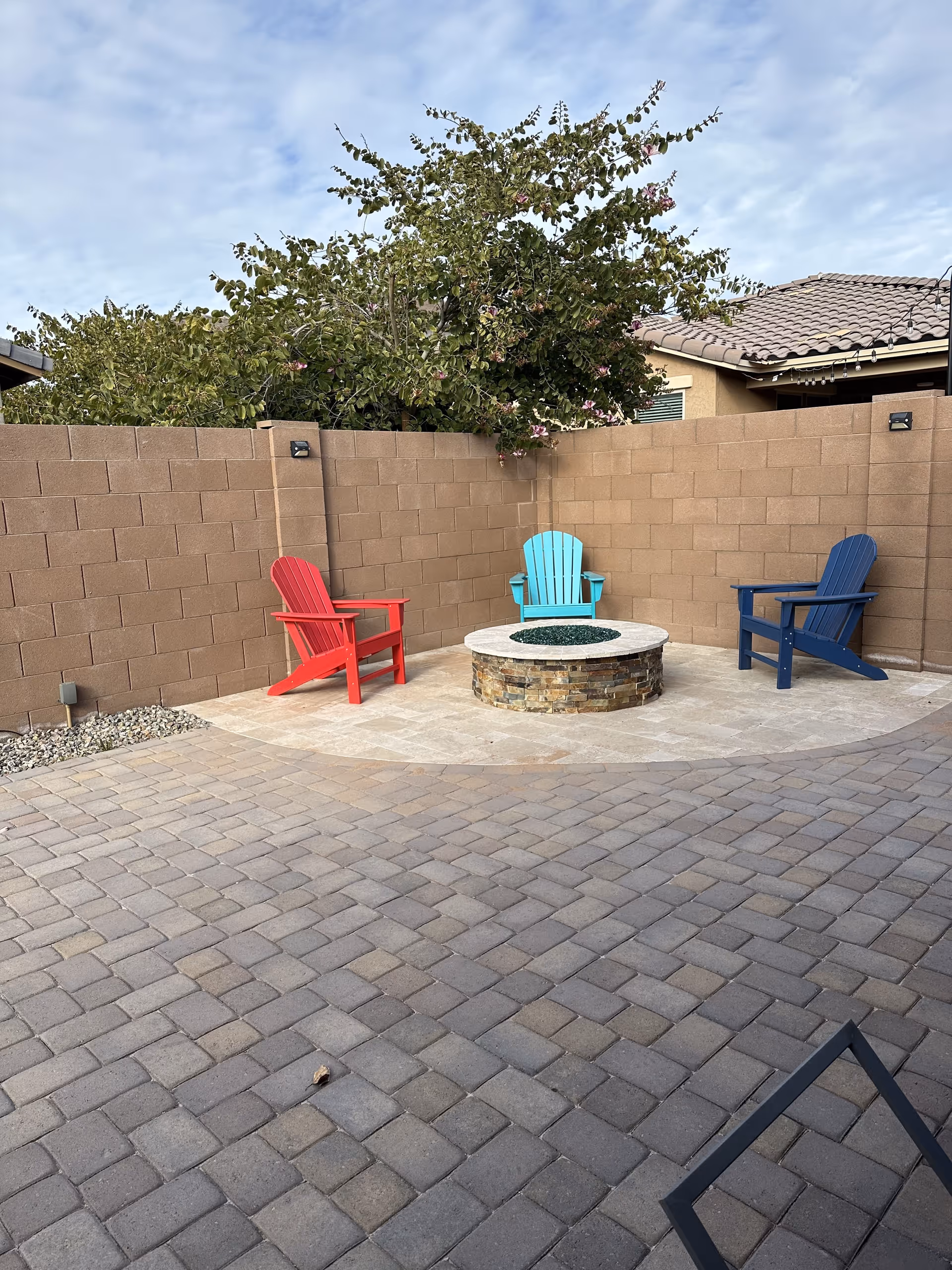 Outdoor courtyard with colorful Adirondack chairs around a stone fire pit.