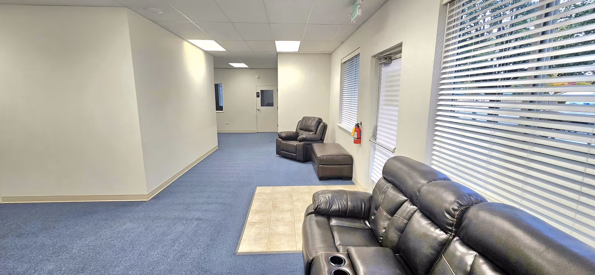 A long blue-carpeted interior hallway in a senior living facility with leather recliners.